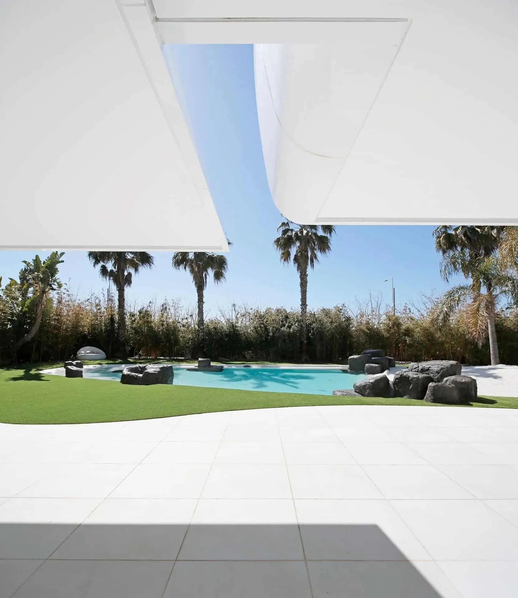 雕塑式白色立面，配有遮阳棚，面向后院的有机泳池