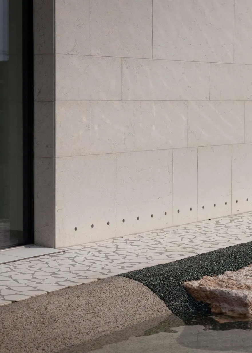 Pared exterior de piedra beige lisa con elementos arquitectónicos modernos, fachada minimalista de edificio, arquitectura exterior contemporánea, superficie de concreto limpia, diseños arquitectónicos con revestimiento en piedra