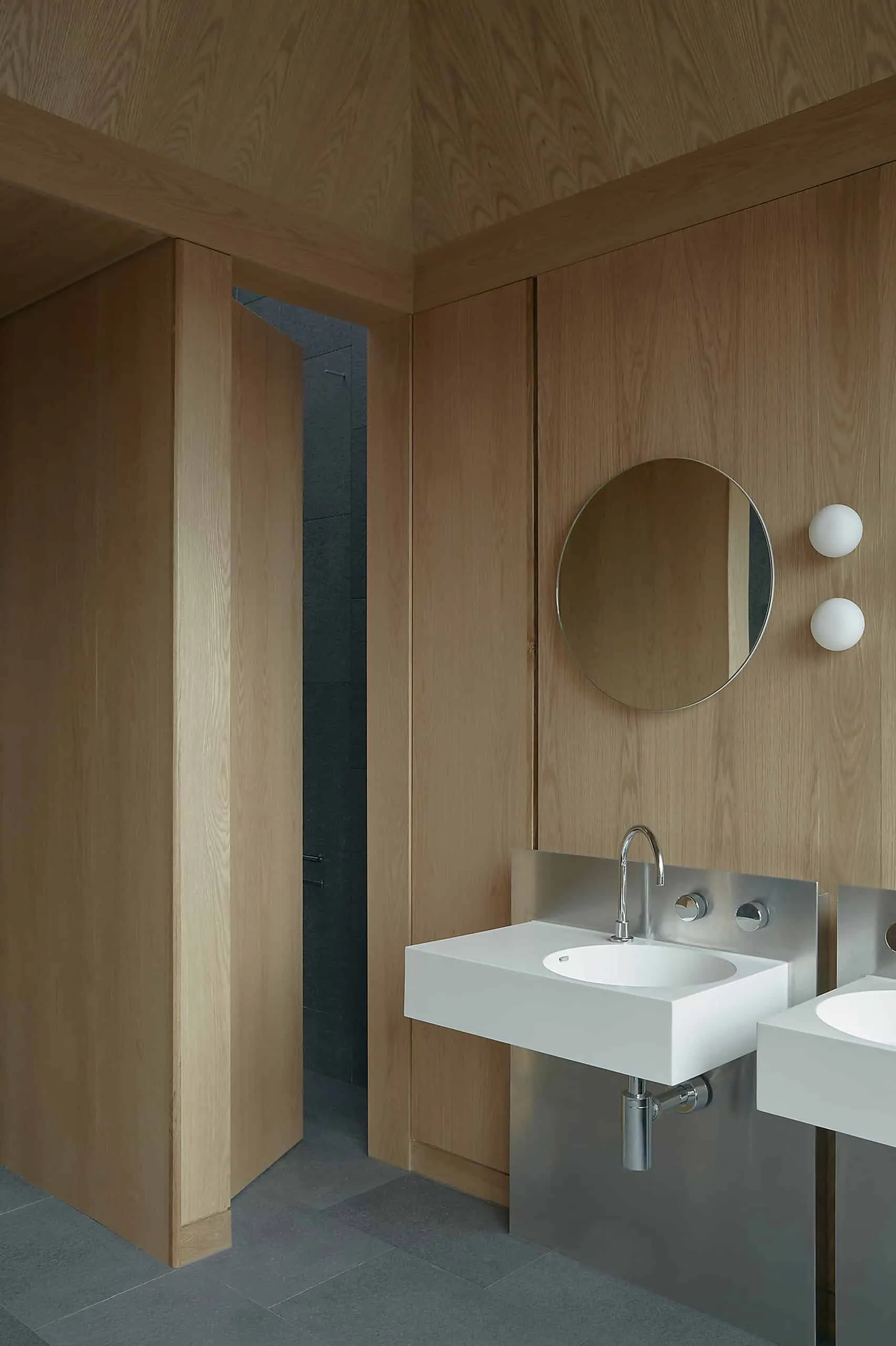 Modern stylish bathroom with wooden walls, minimalist white sink and round mirror for modern architectural interior.
