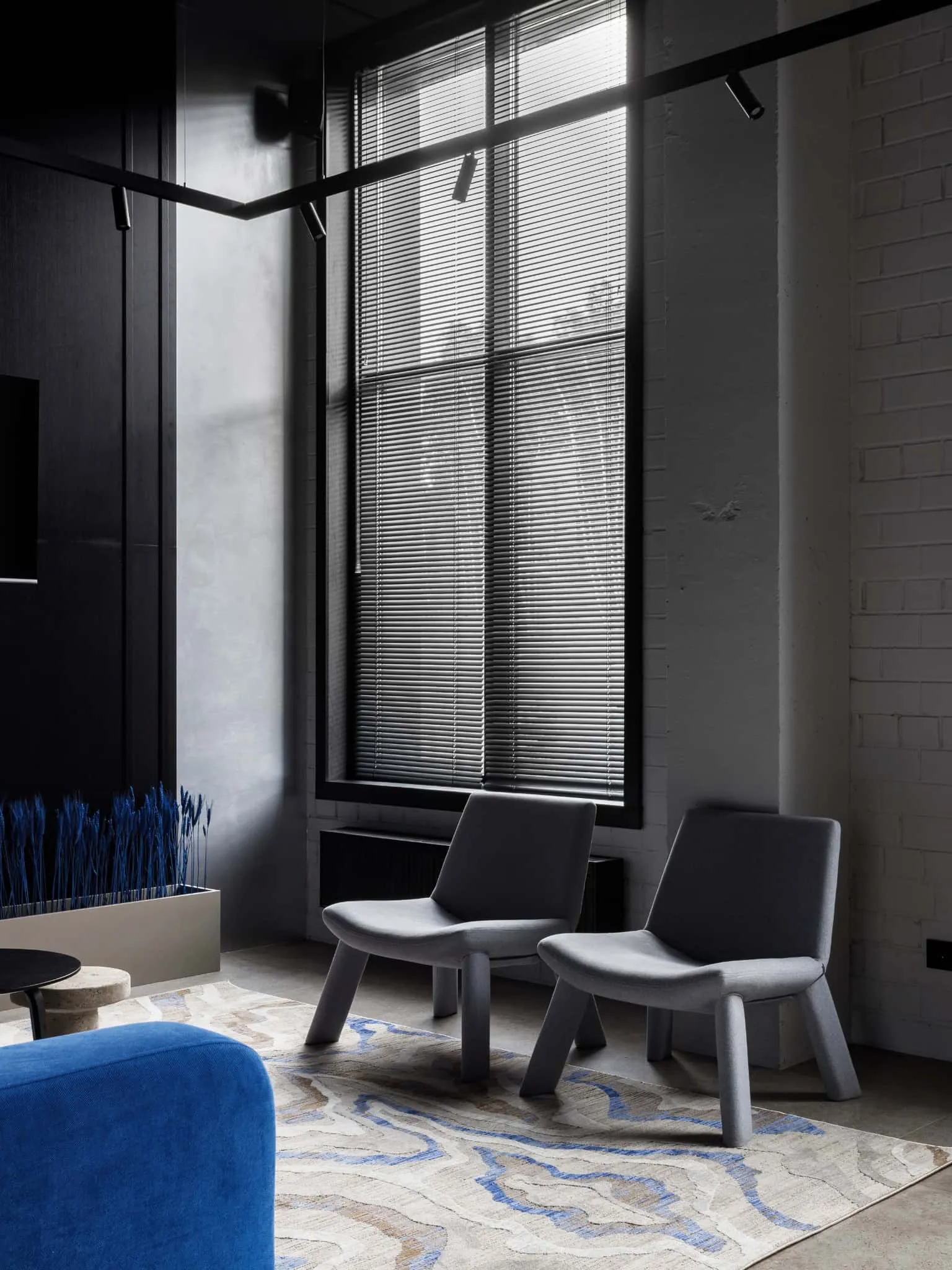 Modern interior with minimalist black and gray chairs by the large window with horizontal blinds, showing elegant architectural elements and stylish decoration.