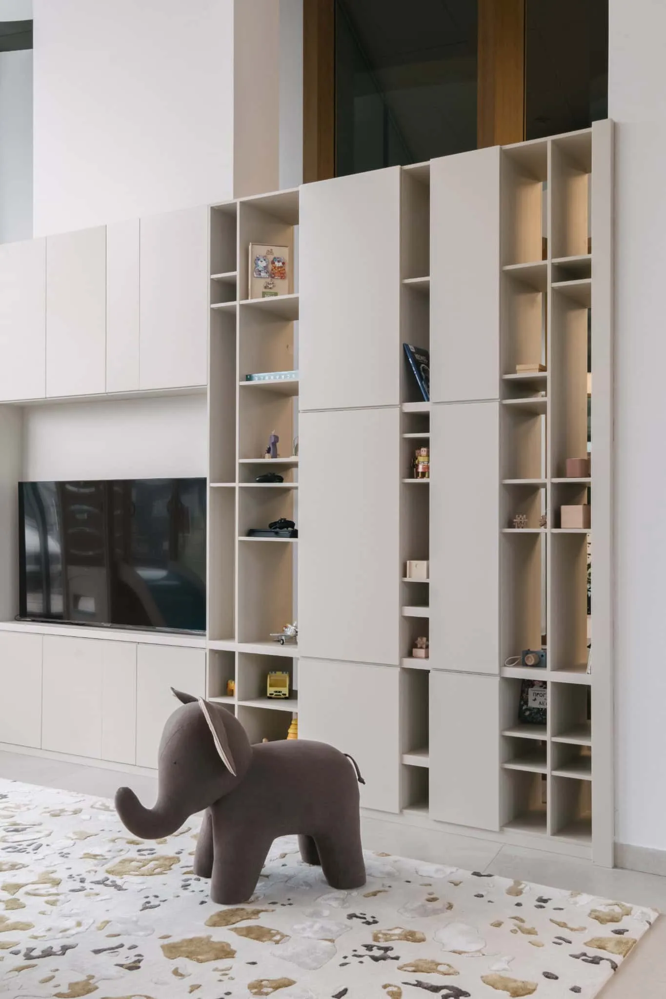 Scandinavian modern living room with minimalist white built-in shelf and fluffy elephant toy, featuring sleek design and functional storage solutions.