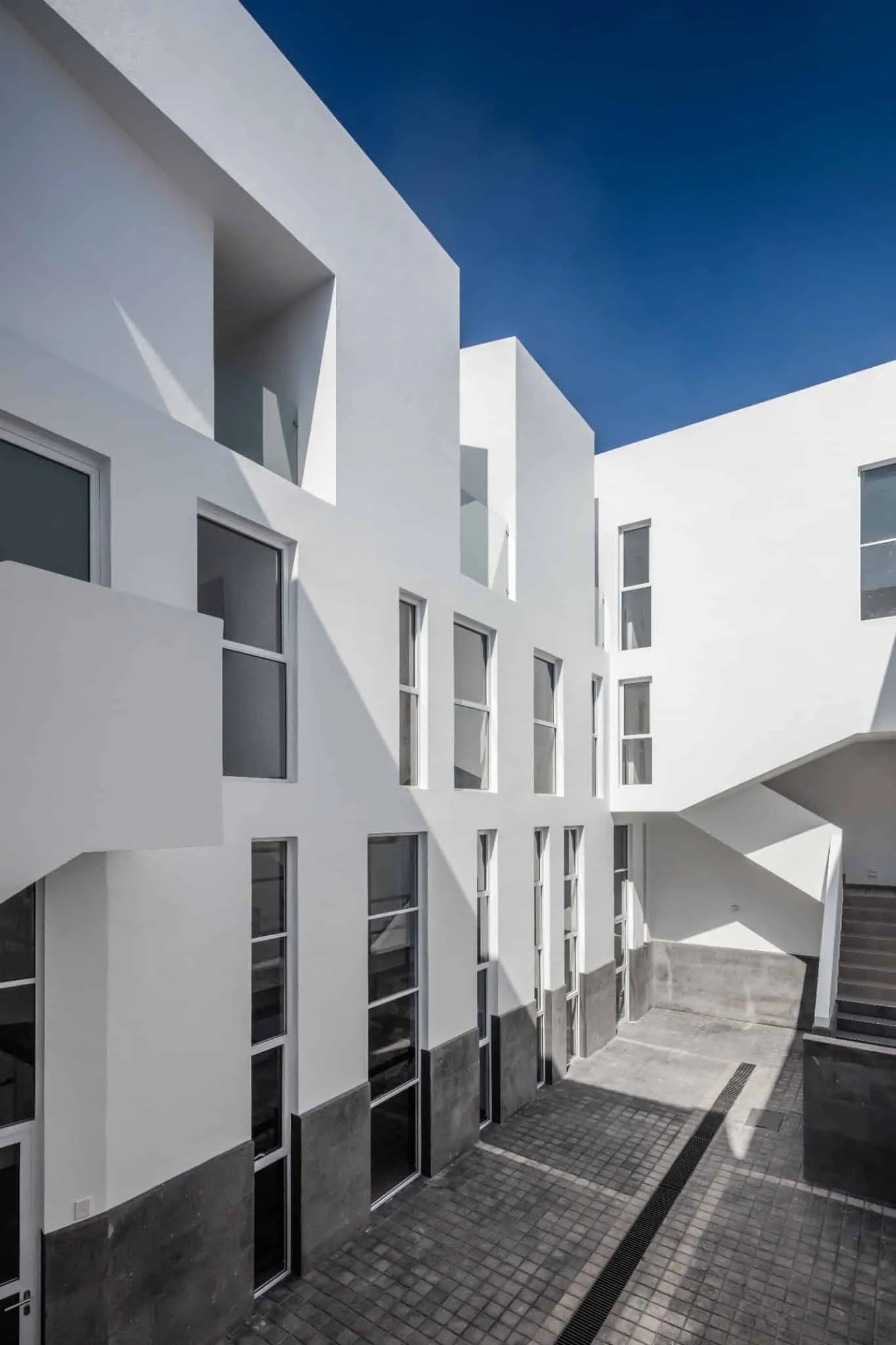 MM34 – Мар Медитерранео 34 от Ателье Инка Эрнандес — внутренний фасад двора с белыми объемами и серым каменным основанием, Такуба, Мехико