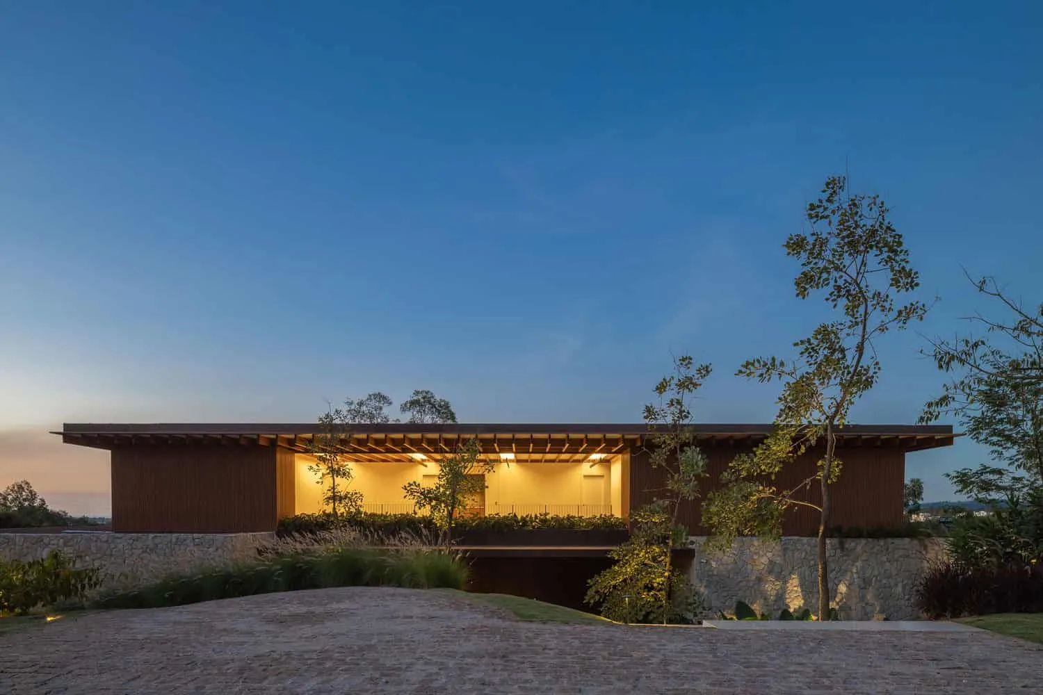 现代极简住宅，弯曲屋顶与天然材料，坐落在景观花园中。可持续建筑结合优雅设计和温暖照明，融合内外居住空间。