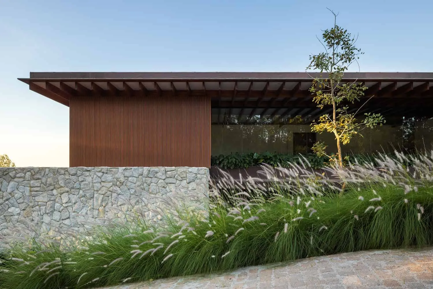 现代住宅，木制立面与大窗户，被景观花园环绕，装饰有草本植物和树木。