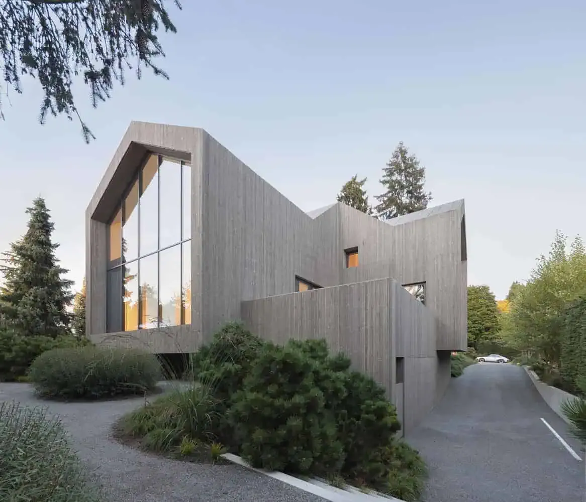 Modern minimalist concrete house with large glass windows, surrounded by lush greenery and natural landscape, showcasing contemporary architecture design.