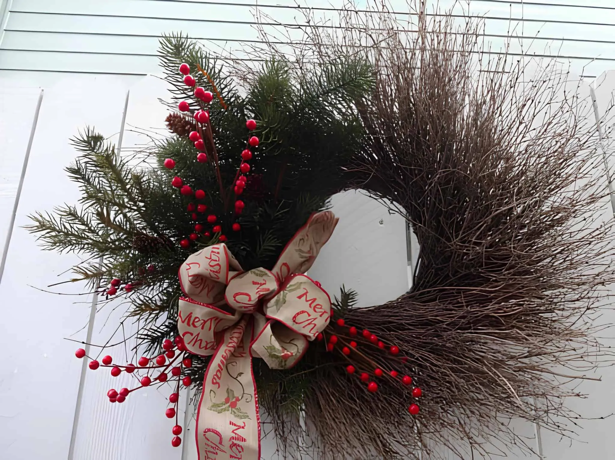 Asymmetrische Zweig- und immergrüne Krone mit Weihnachts-Schleife Asymmetrische Weihnachtskranz aus Zweigen und immergrünen Pflanzen mit roten Beeren sowie einer festlichen Schleifen-Schleife
