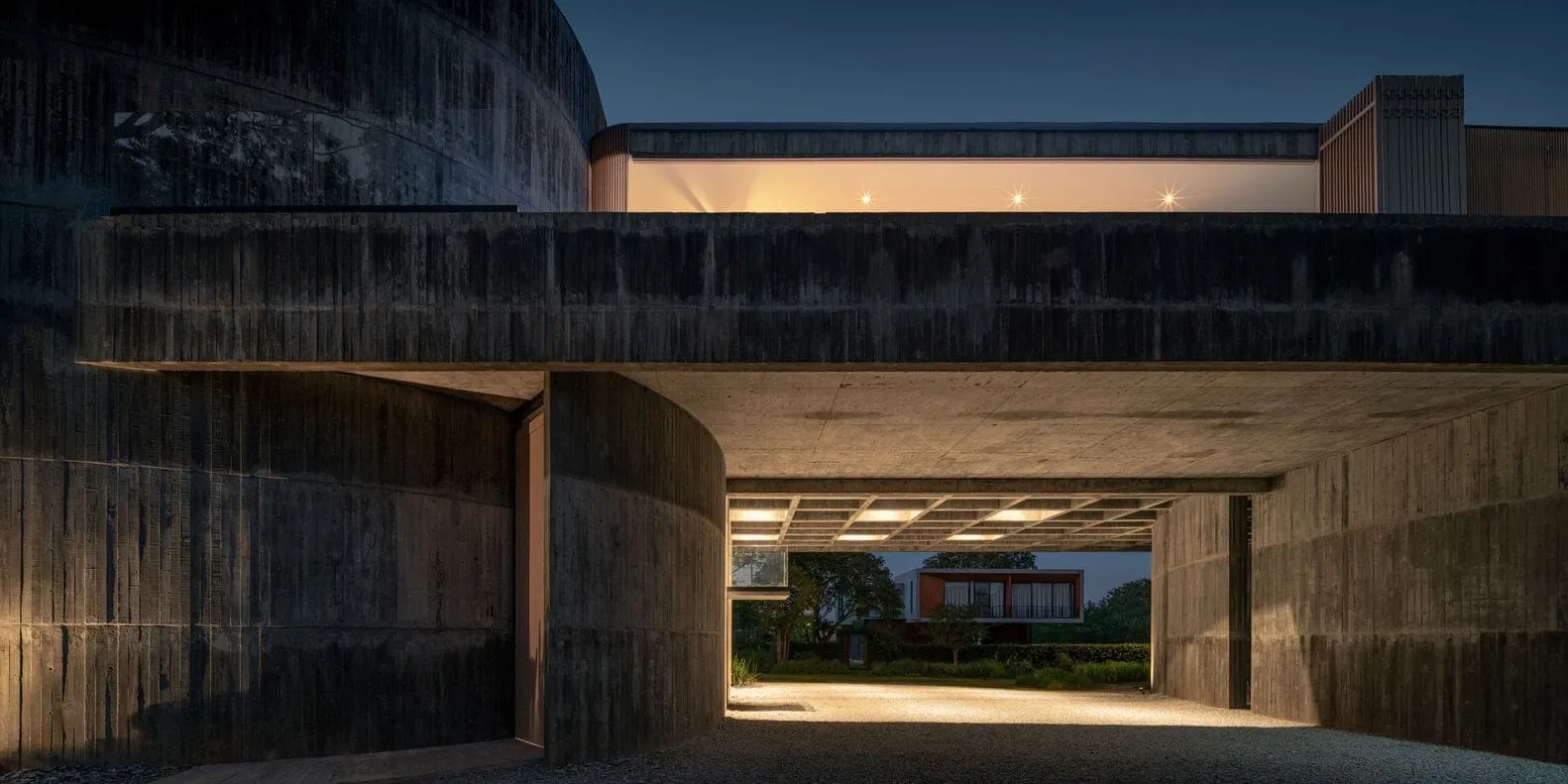 Eingang zur W House II bei Nacht – gebogene Betonwand von IDIN Architects Nächtlicher Eingang der W House II in Thailand, umrahmt von einer gebogenen Betonwand, entworfen von IDIN Architects