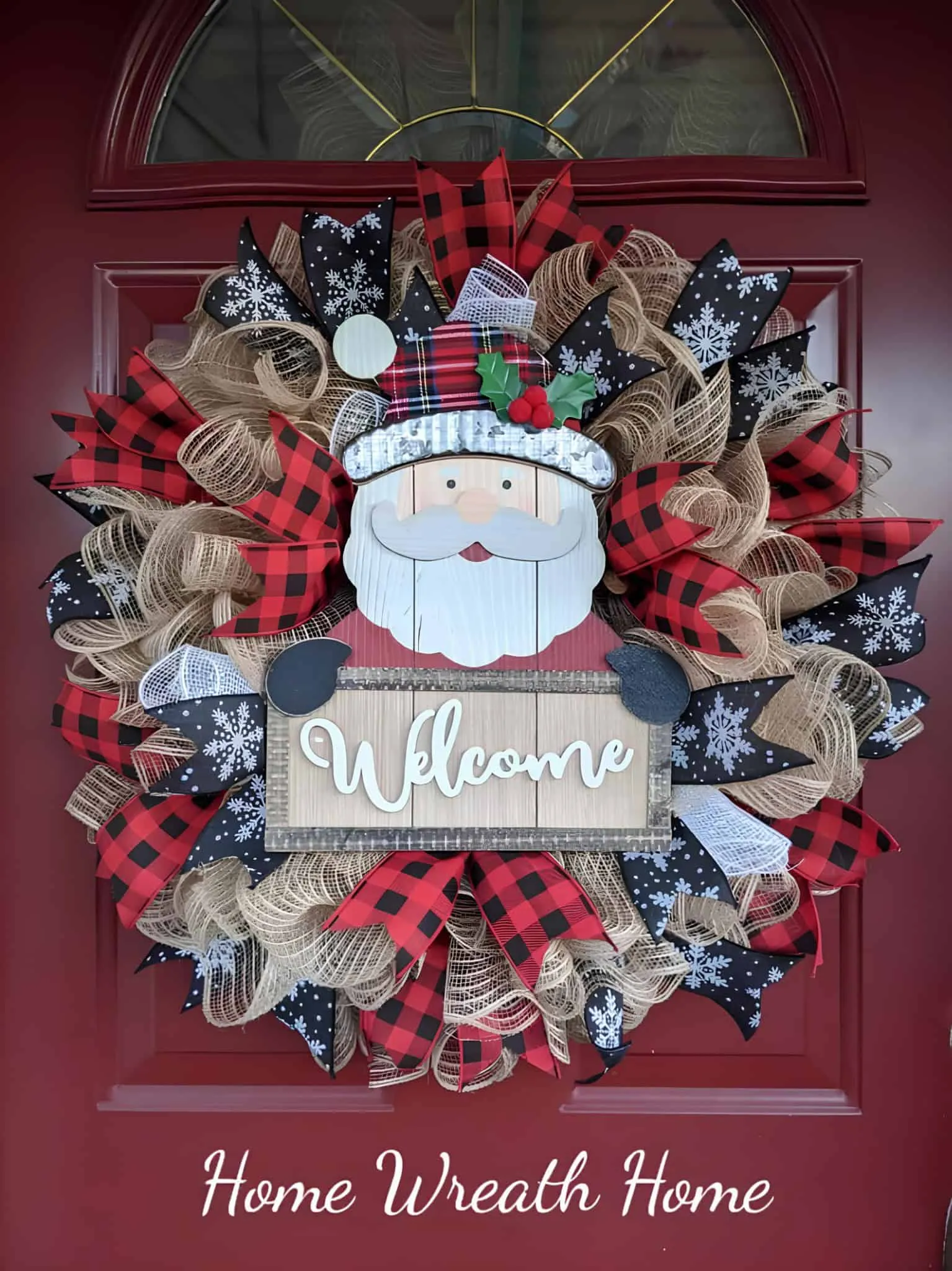 Begrüßungskranz mit Santa im Karomuster Farbenfroher Weihnachtskranz mit dem Gesicht von Santa Claus, Karomuster sowie Schneeflockenbändern – dekoriert an einer roten Haustür für die Weihnachtsdekoration des Zuhauses.