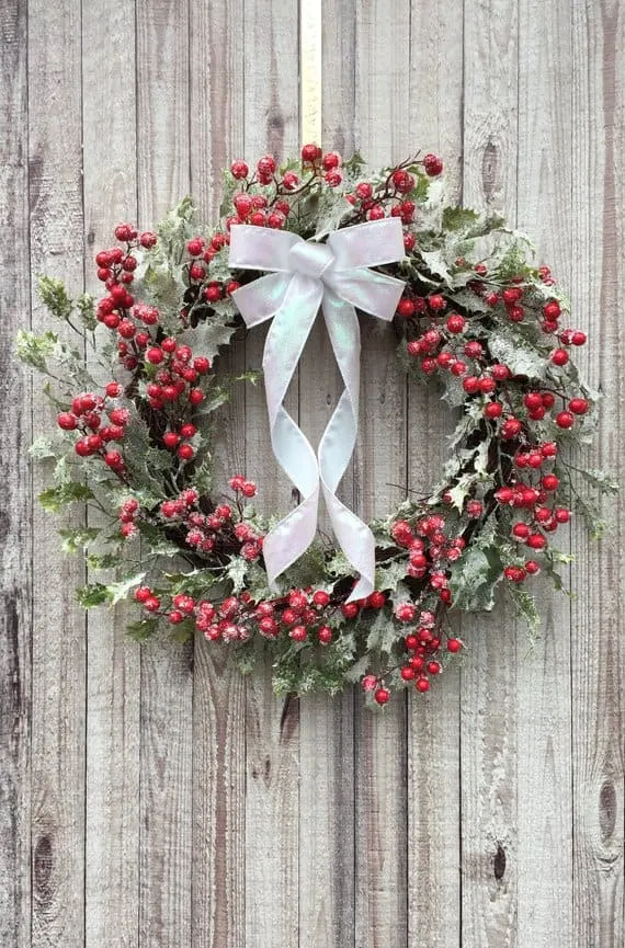 Kränz aus gefrorenen Beeren mit weißer Schleife Mit Schnee bedeckter Weihnachtskränz aus Beeren mit weißer Satinschleife