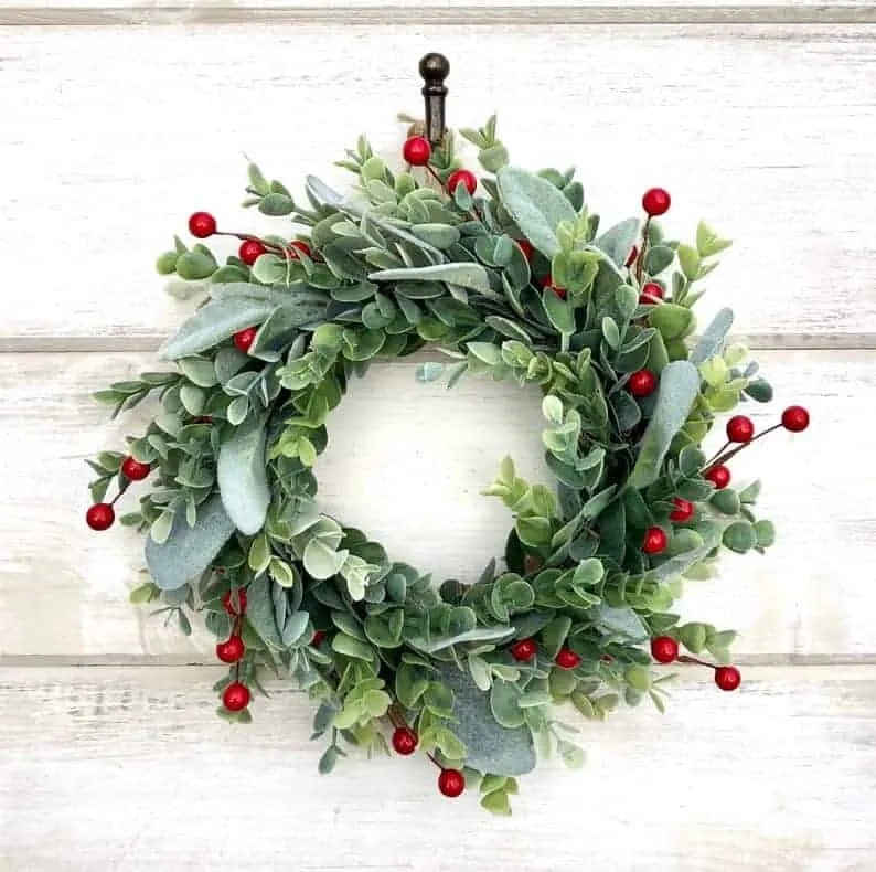Eucalyptus Green Berry Wreath Weihnachtskranz aus Eukalyptus mit roten Beeren an einer weißen Wand