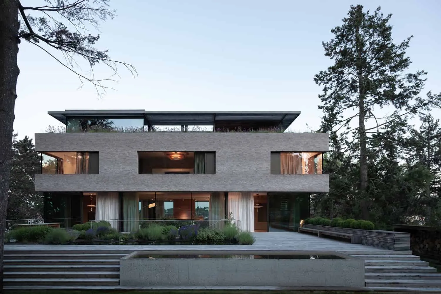 Vorderansicht der Villa Vista am Abend mit Teich von Znameni Ctyr Architekti Villa Vista von Znameni Ctyr Architekti, Vorderansicht bei Dämmerung mit spiegelndem Teich und Stufen in Prag