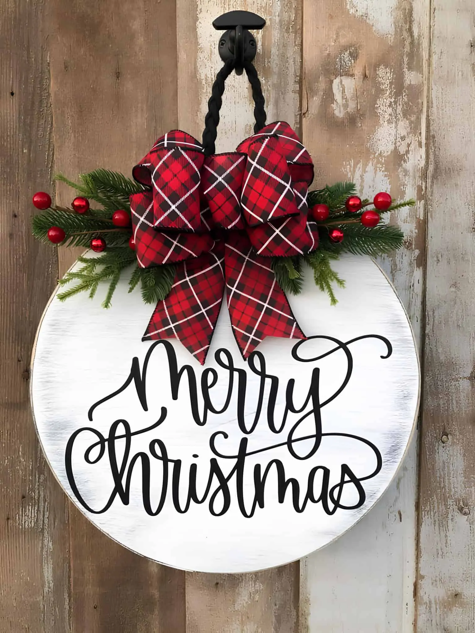 Runder Weihnachts-Schild mit Schriftzug und Plaid-Binde Weißer runder Holz-Weihnachts-Schild mit roter Plaid-Binde und immergrünen Pflanzen
