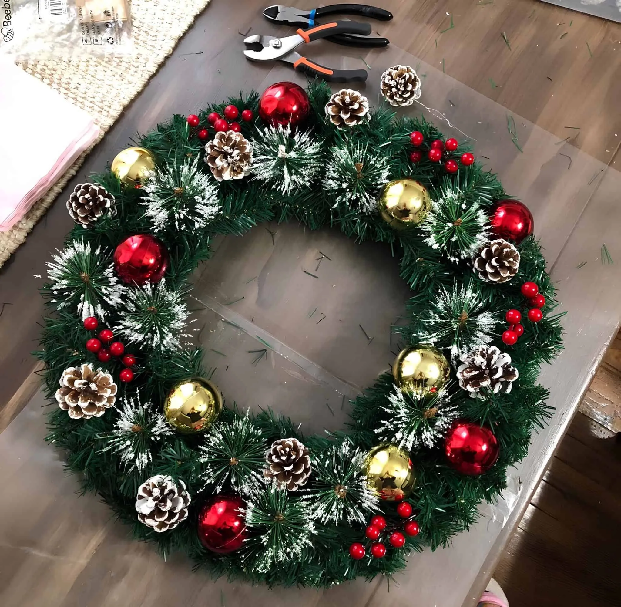 Gold- & Rotdekorierte Kiefernzapfen-Weihnachtskrone Selbergemachte Weihnachtskrone mit goldenen und roten Verzierungen, mit Reif überzogenen Kiefernzapfen sowie roten Beeren