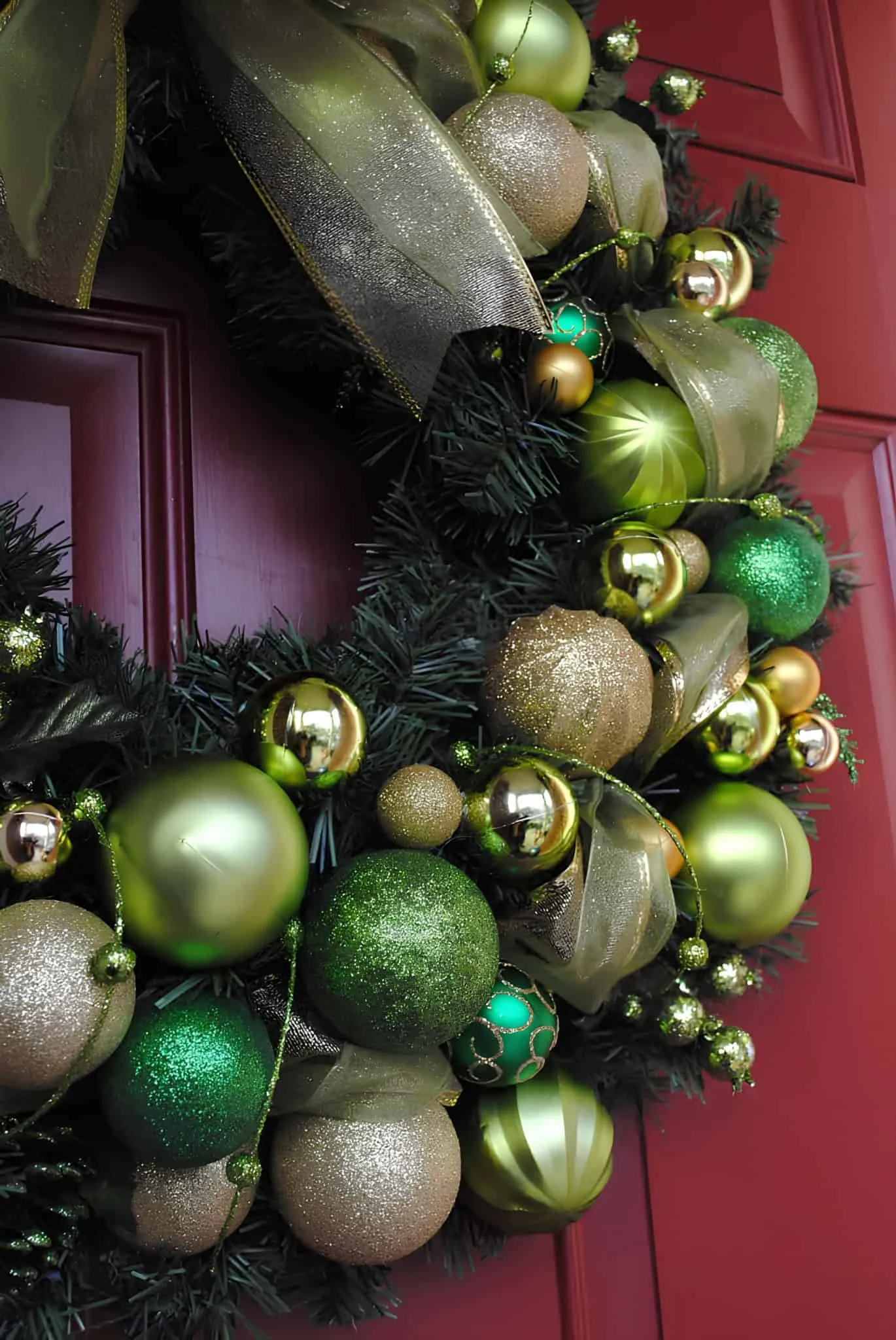 Grüne und goldene Dekorationsweihnachtskrone Grüne und goldene Weihnachtskrone mit durchsichtiger Schleife an einer roten Tür