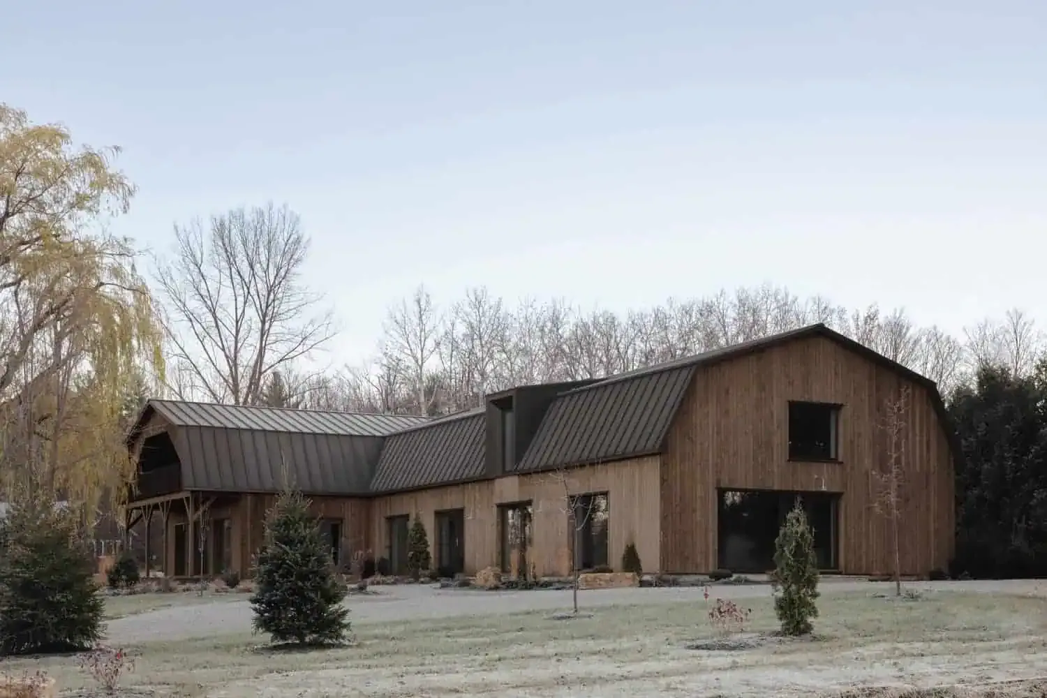 Ein rustikales, modernes Holzhaus mit Metalldach, umgeben von Bäumen und einem gestalteten Garten, das innovative Architektur sowie nachhaltiges Design zeigt.