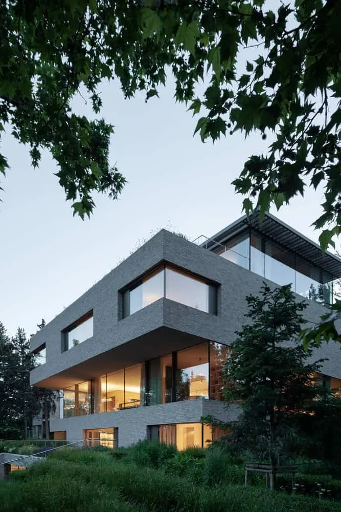 Villa Vista – abgeschnittene Ziegelbauten im Abendlicht von Znameni Ctyr Architekti Villa Vista von Znameni Ctyr Architekti: abgeschnittene Ziegelbauten mit leuchtenden Innenräumen bei Dämmerung in Prag