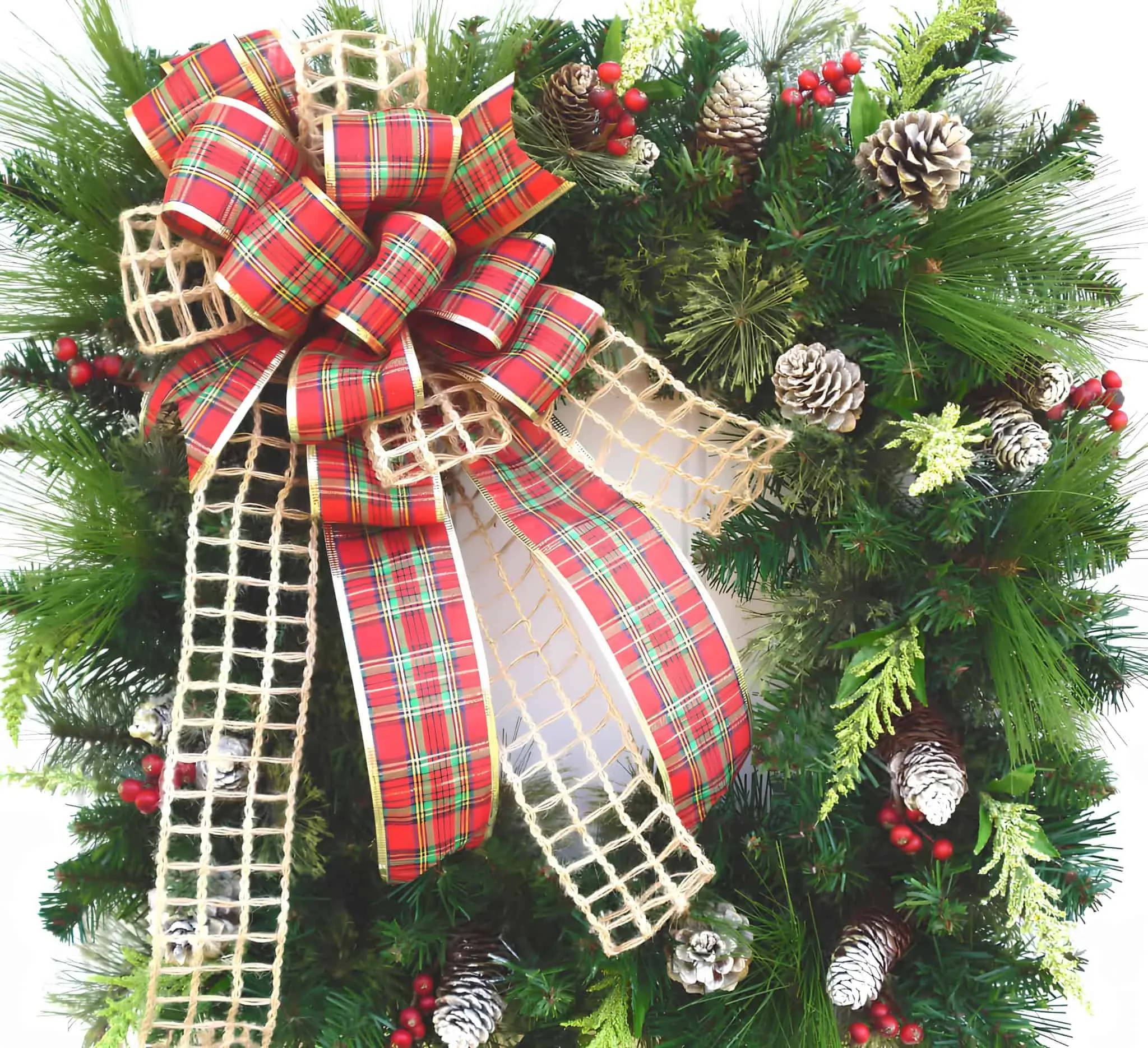Weihnachtskranz mit karierter Schleife und Kiefernnüssen Klassischer immergrüner Kranz mit kariertem Schleifchen, Kiefernnüssen und roten Beeren