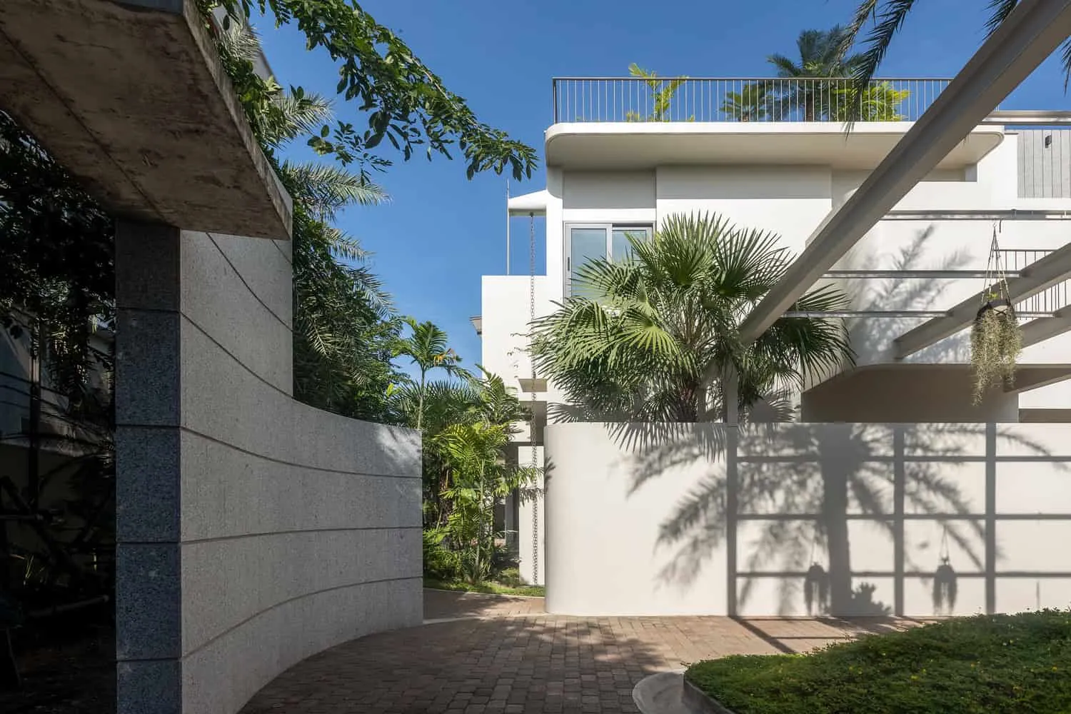 Wat Bo House mit geschwungener Einfahrt und Palmenschatten von UAD Architects Wat Bo House von UAD Architects – geschwungene Einfahrtswand sowie Einfahrt mit Palmenschatten in Kambodscha