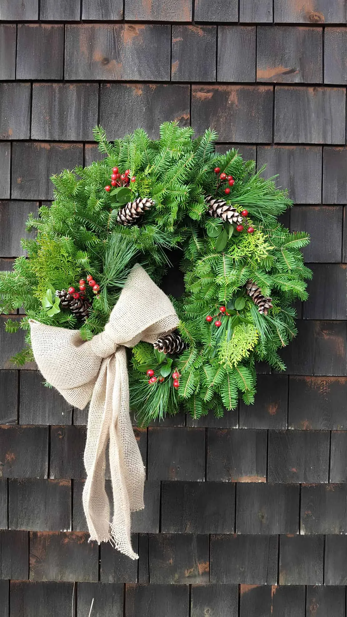 Rustikaler Sacktuch-Bogen – Immergrüner Kränzchen Immergrüner Weihnachtskranz mit Sacktuch-Bogen, Kiefernzapfen und roten Beeren