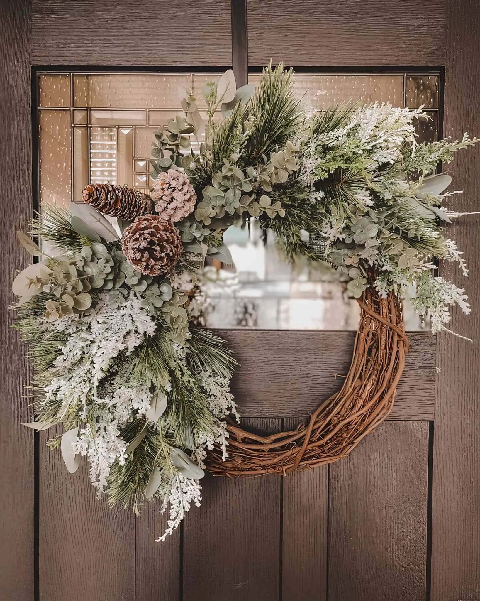 Holzkranz zum Weihnachtsfest aus gefrorenem Eukalyptus und Kiefernzapfen Halbbedeckter Holzkranz in Form einer Rebenranken mit gefrorenem Eukalyptus, Kiefernzweigen und schneeweißen Kiefernzapfen