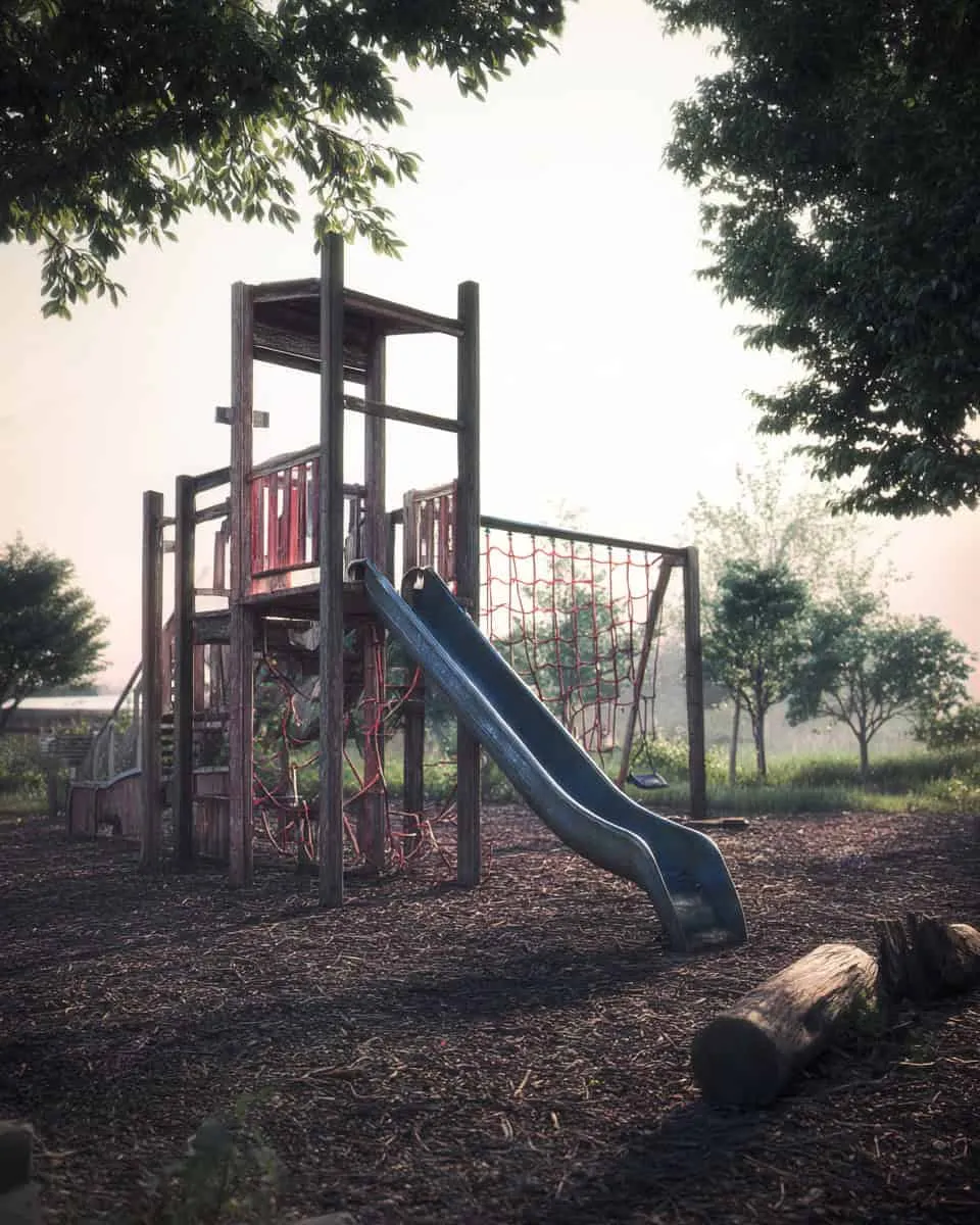 Aged wooden playground with slide and climbing net in a park setting on a foggy morning.
