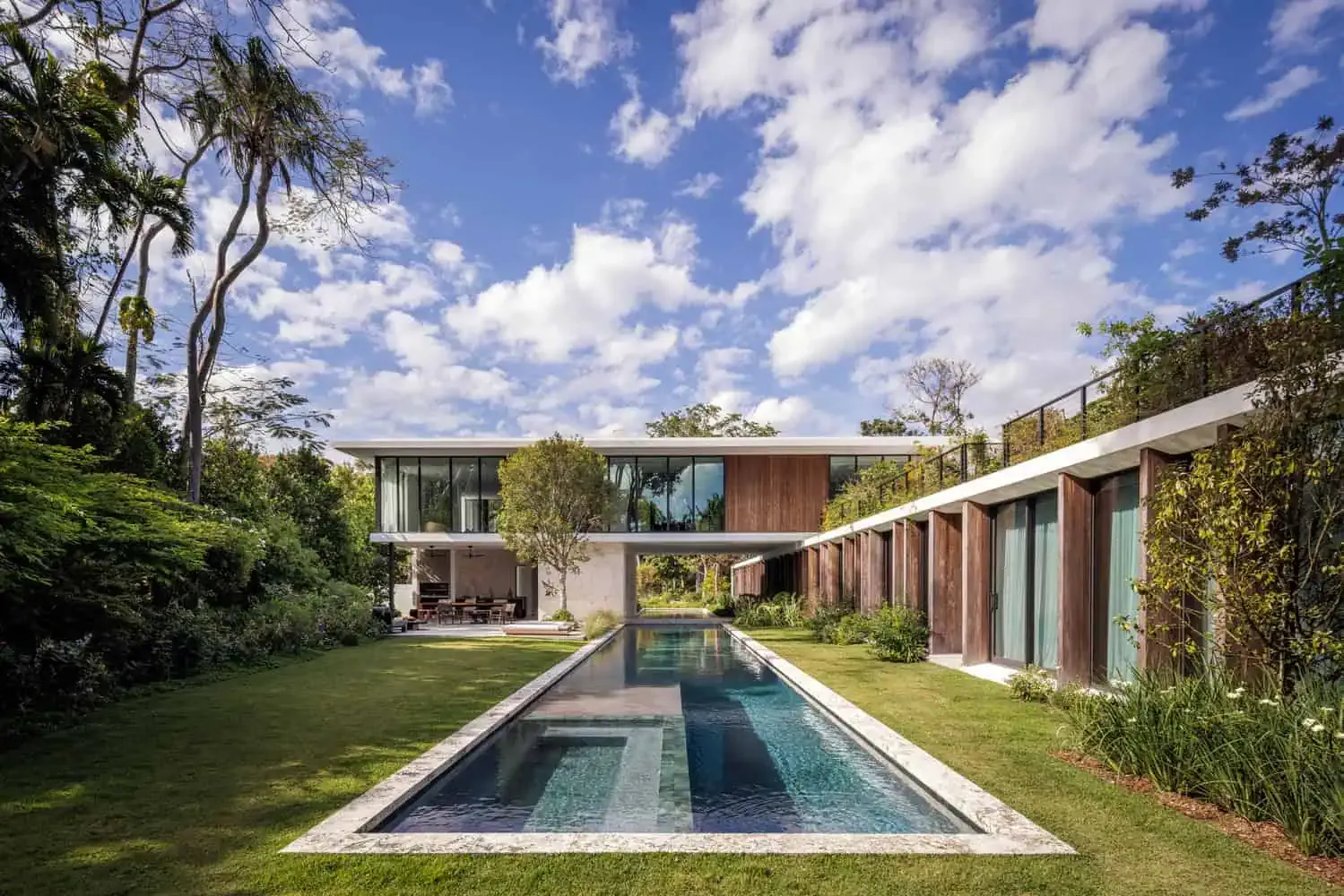 Ein modernes Luxushaus mit ansprechendem Design, Glaswänden und Außenpool in einem üppigen tropischen Garten – ein Beispiel für zeitgenössische Architektur und künstlerisches Design.