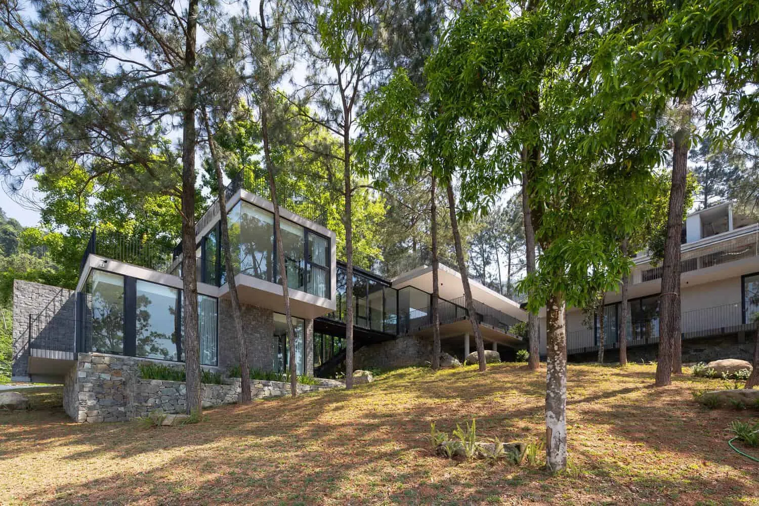 Tam Dao Retreat House – Waldfassade am Hang von Idee architects Tam Dao Retreat House von Idee architects: Glas- und Steinfassade am Waldrand auf einem Hang in Tam Dao, Vietnam