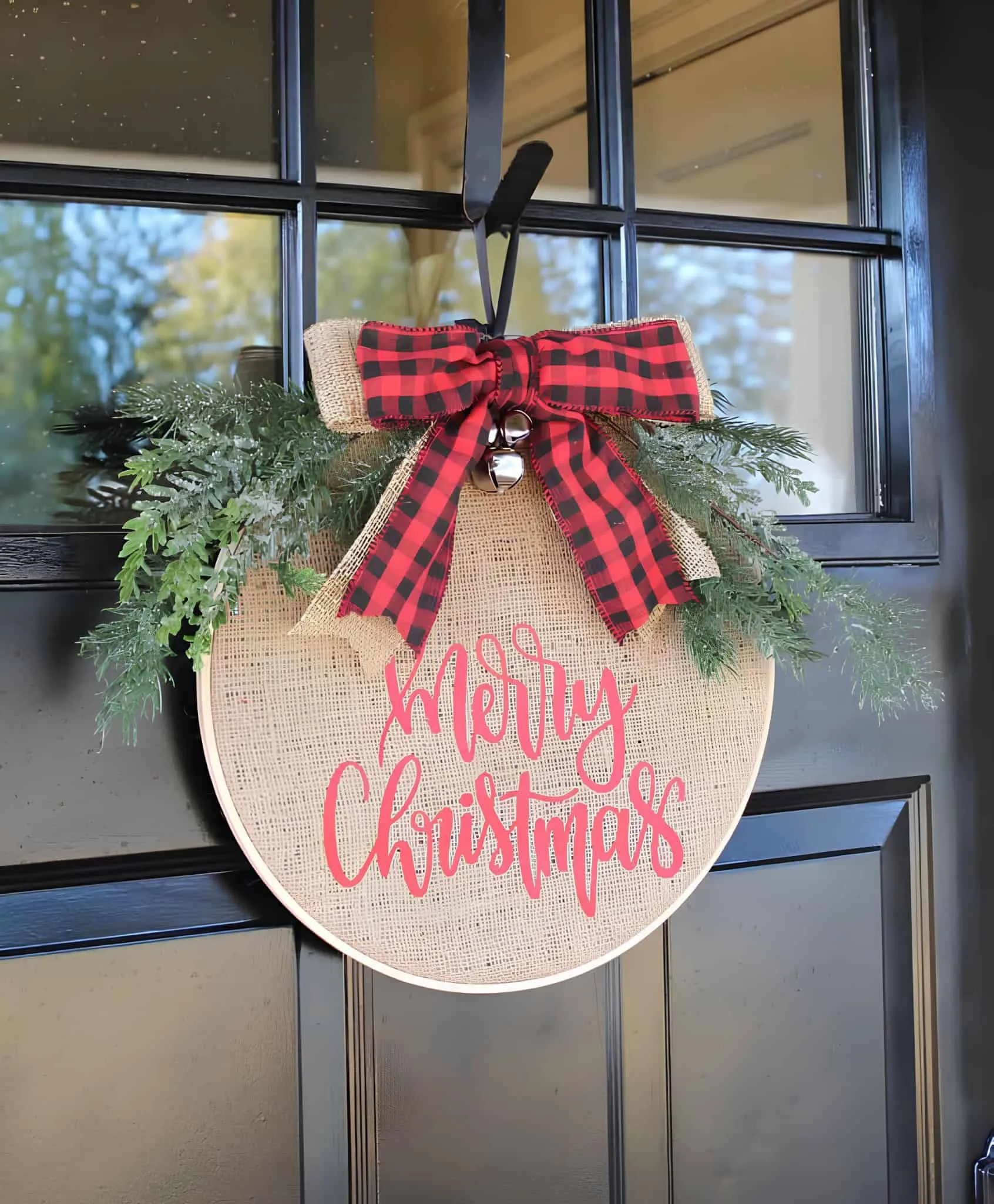 Runder Schild aus Jute mit Buffalo-Plaid-Binde Runder Türhänger aus Jute zum Thema Frohe Weihnachten mit Buffalo-Plaid-Binde, Grünzeug und Glöckchen