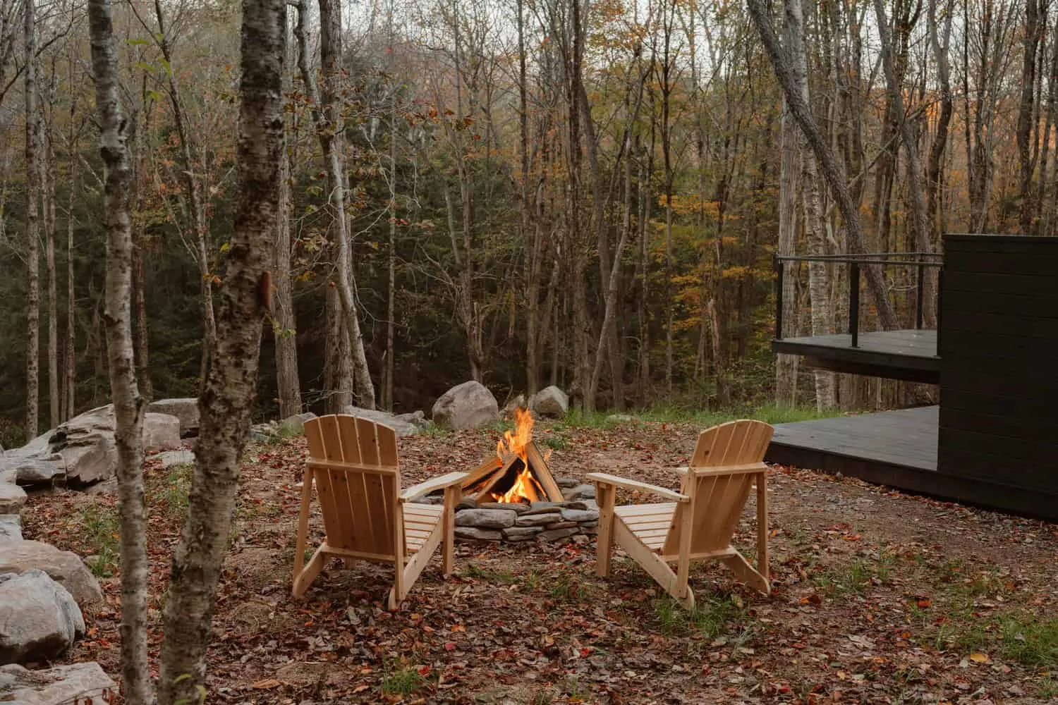 Feuerstellebereich mit Holzstühlen in einer Lichtung im Wald neben dem Forest Edge House in New York