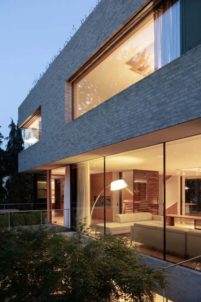 Wohnzimmer der Villa Vista bei Dämmerung von Znameni Ctyr Architekti Villa Vista von Znameni Ctyr Architekti, Abendansicht des verglasten Wohnzimmers mit warmem Innenlicht