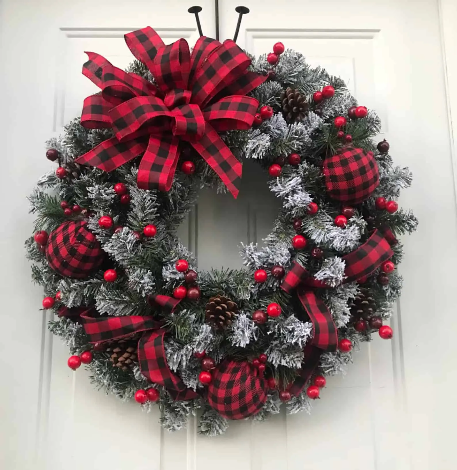 Weihnachtskranz im Buffalo-Plaid-Muster mit roten Beeren Weihnachtskranz mit Buffalo-Plaid-Binde und gefroster Grünpflanze sowie roten Beeren