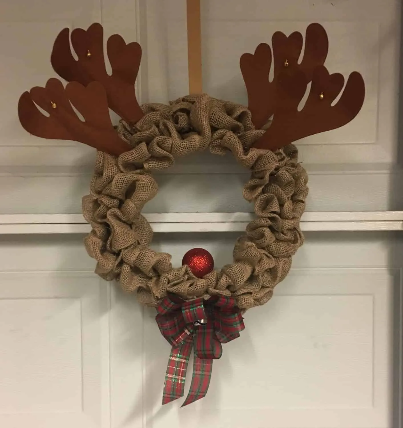 Rentier Rudolph – Weihnachtskranz aus Jute Weihnachtskranz aus Jute im Rudolph-Stil mit Hörnern, roter Nase und kariertem Band