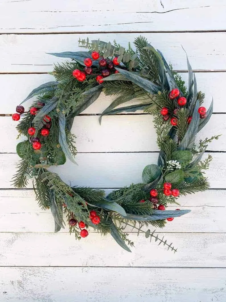 Minimalistisches Kränzchen aus immergrünen Pflanzen und Eukalyptusbeeren Minimalistisches Weihnachtskränzchen aus immergrünen Pflanzen und Eukalyptus mit roten Beeren