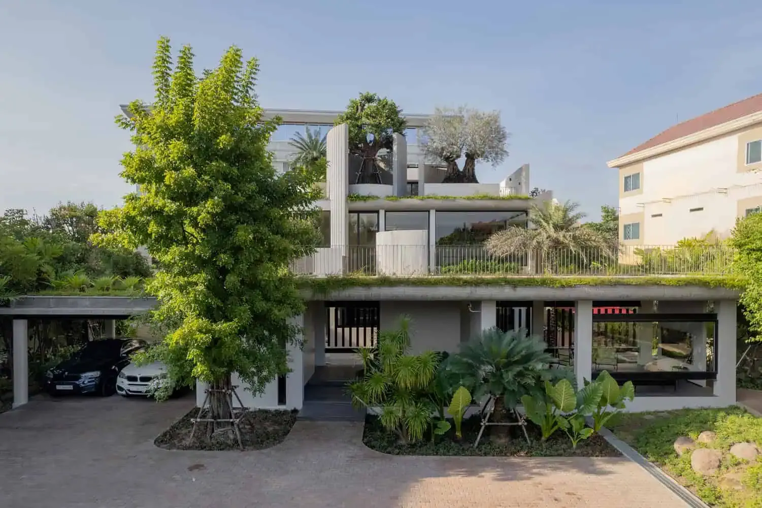 Ein modernes Luxushaus mit zeitgenössischer Architektur, das durch klare Linien, große Glasfenster, üppige Grünpflanzen sowie Dachgärten gekennzeichnet ist und innovatives Wohndesign sowie die Integration in die Landschaft veranschaulicht.