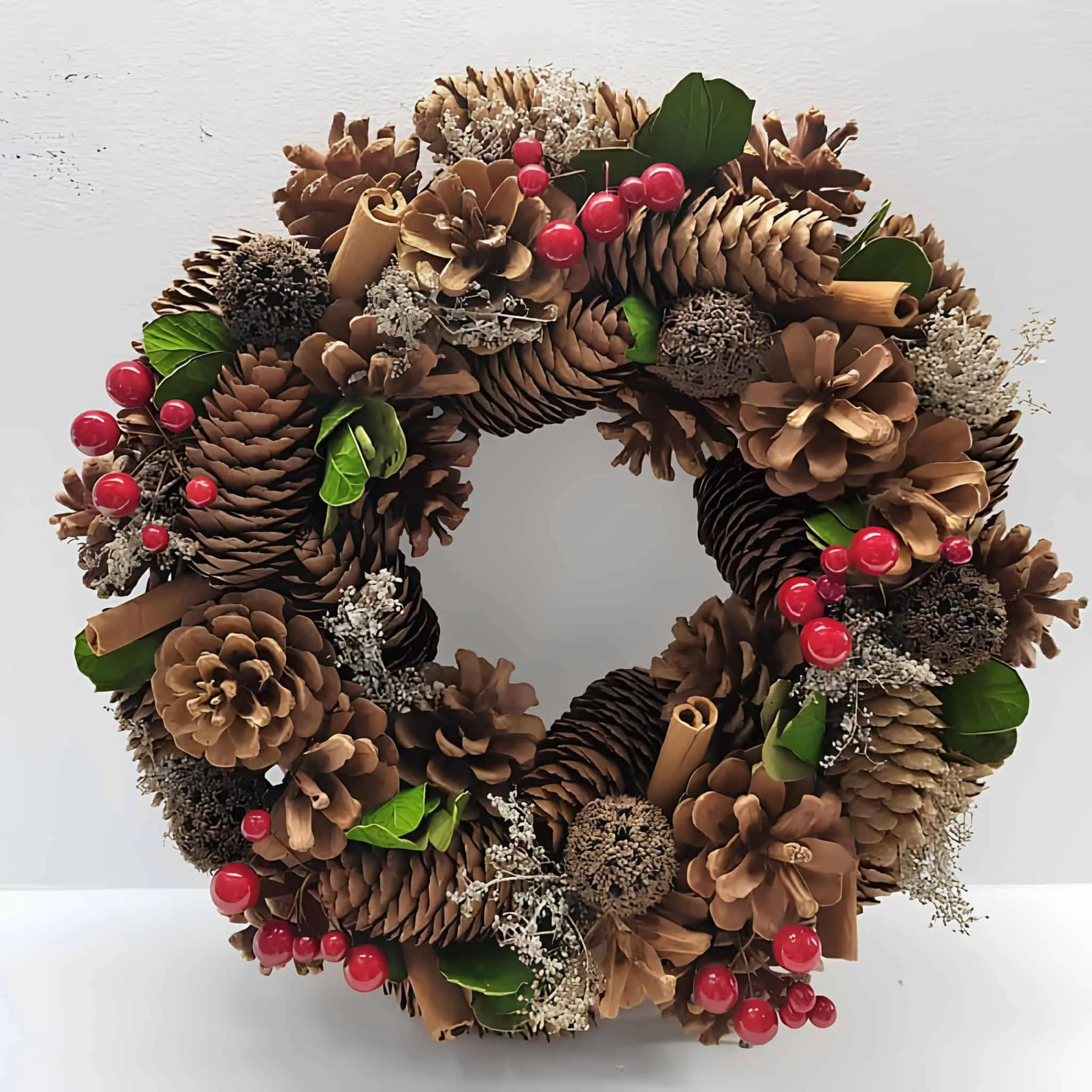 Kiefernzapfenkranz mit Zimt und roten Beeren Weihnachtskranz aus Kiefernzapfen, verziert mit Zimtstangen, roten Beeren und Grünpflanzen