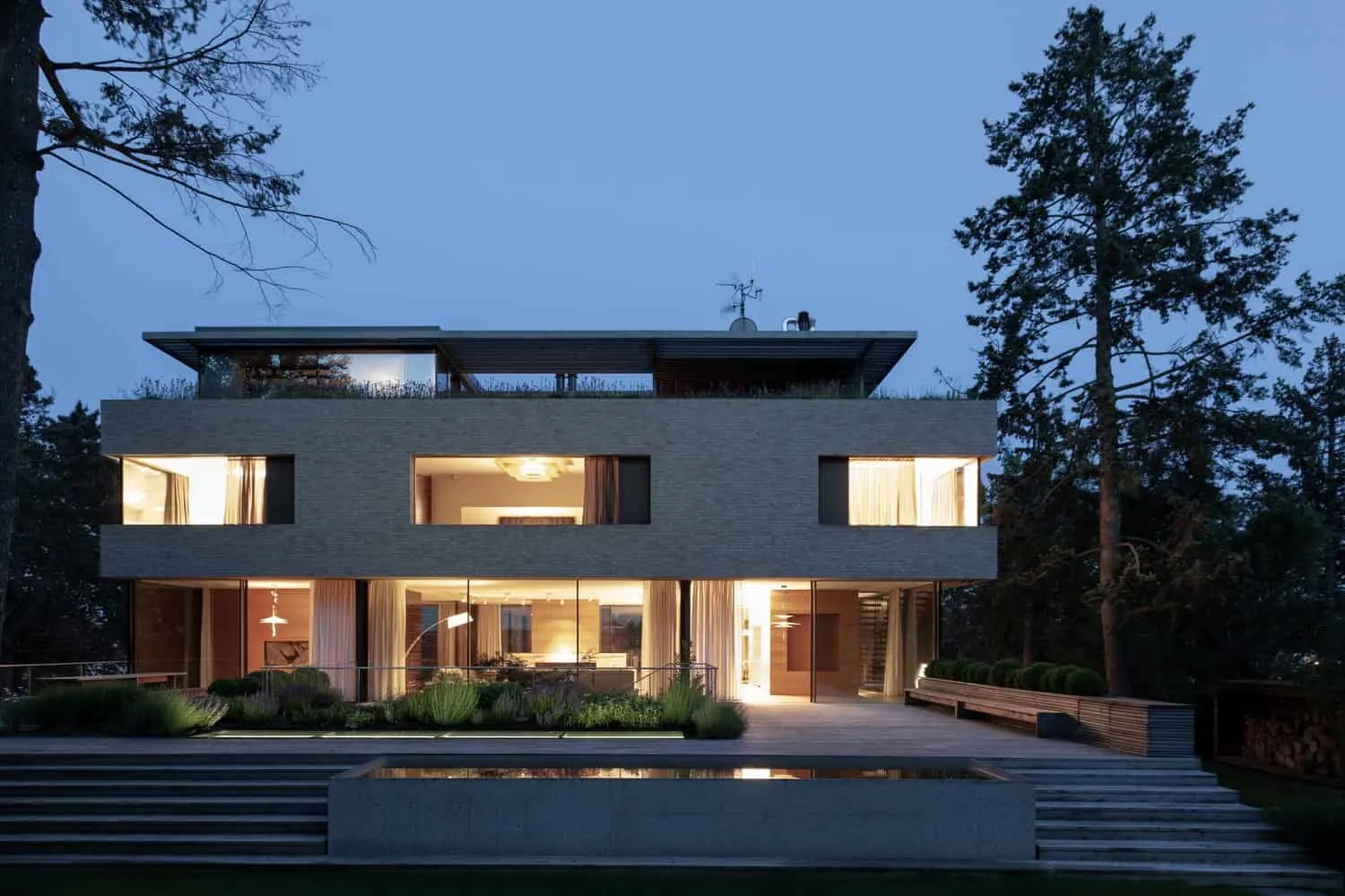 Vorderansicht von Villa Vista bei Dämmerung, beleuchtet von Znameni Ctyr Architekti Villa Vista von Znameni Ctyr Architekti: Vorderansicht bei Dämmerung mit warmem Innenlicht und Spiegelteich