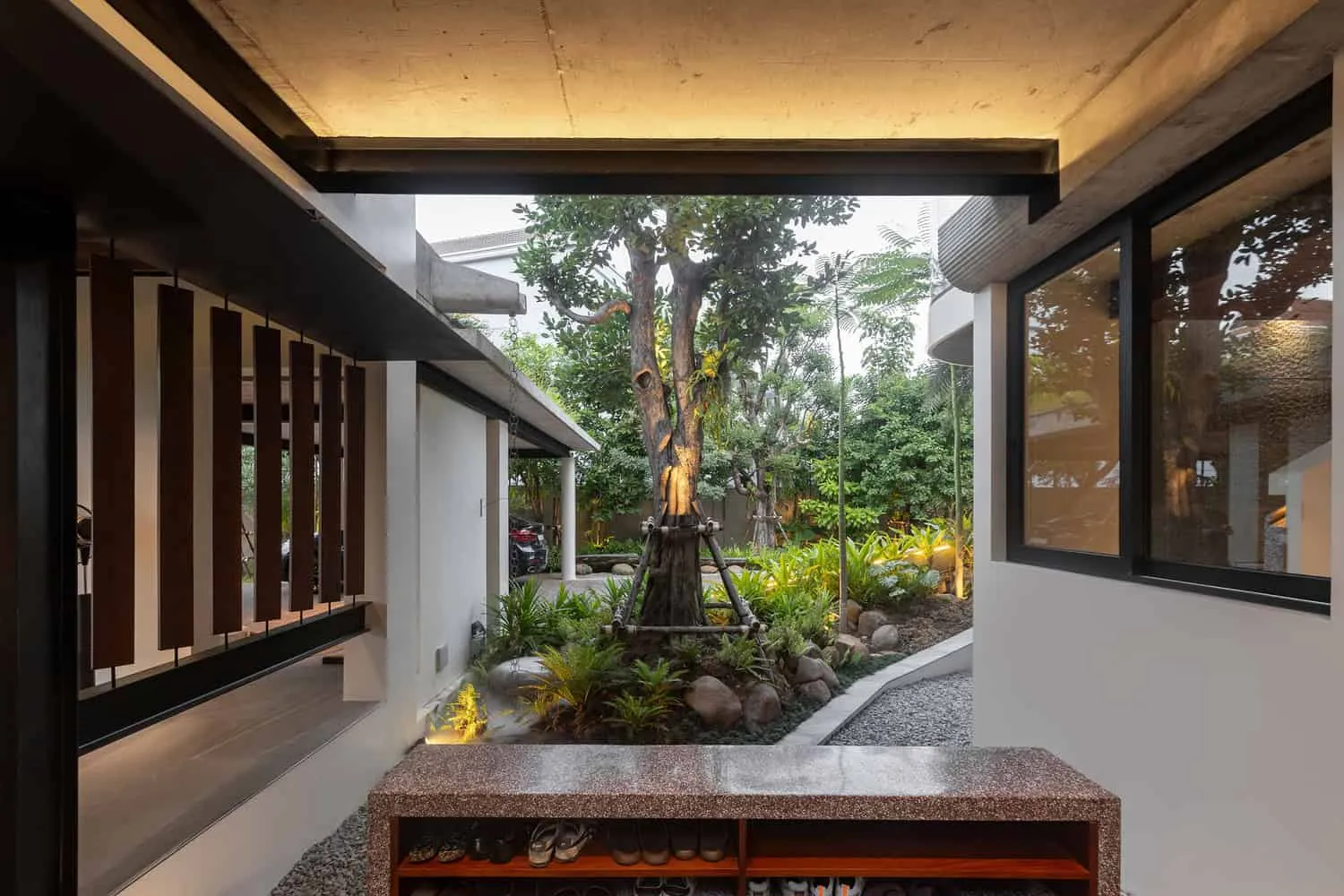 Wat Bo House: überdachter Eingang mit Sitzbank im Garten, entworfen von UAD Architects Wat Bo House von UAD Architects mit überdachtem Eingang, Sitzbank und Blick auf den Garten in Kambodscha