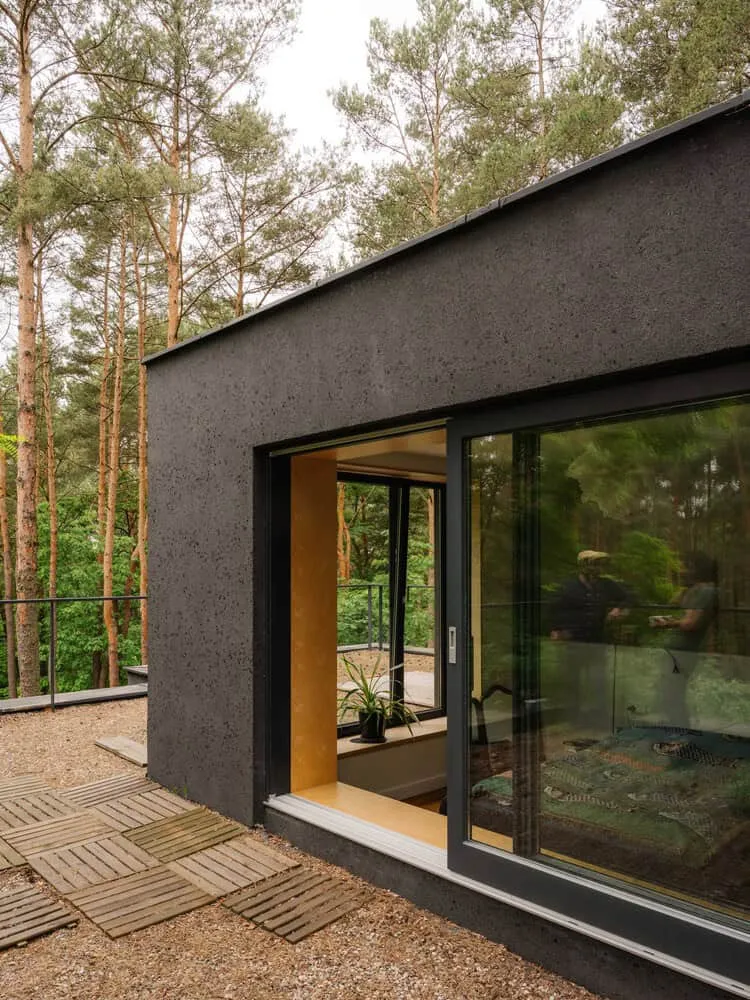 Obenliegendes Eckfenster im Skubianka-Haus von SZCZ Jakub Szczesny Zeitgenössisches kleines Haus aus schwarzem Beton mit großen Schiebeglas-Türen, gelegen in einer Waldumgebung – zeigt moderne Architektur sowie umweltfreundliche Designelemente.