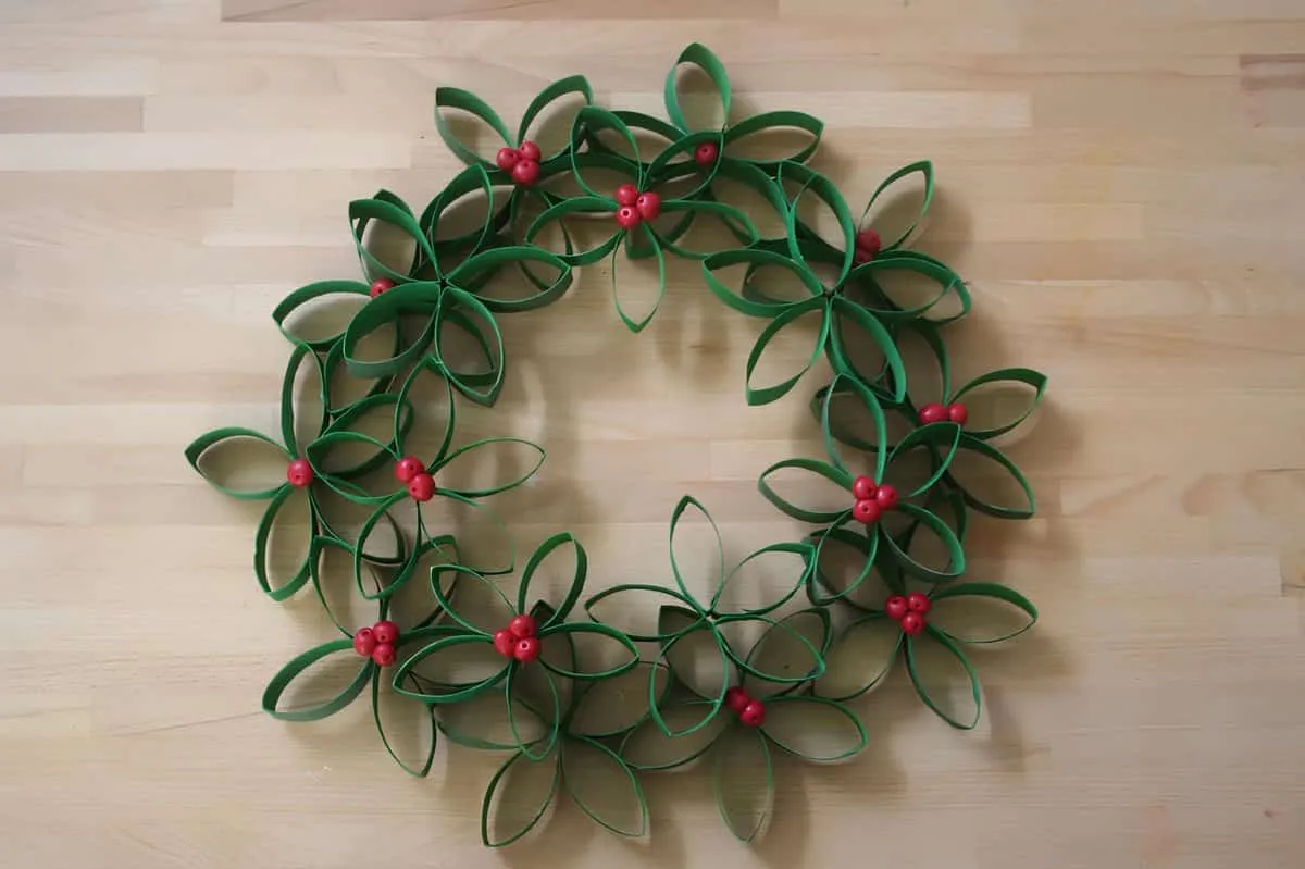 Weihnachtskranz aus Papierrollenblumen Handgefertigter Weihnachtskranz aus bemalten Papierrollen, die zu Blumen geformt wurden und rote Beeren haben