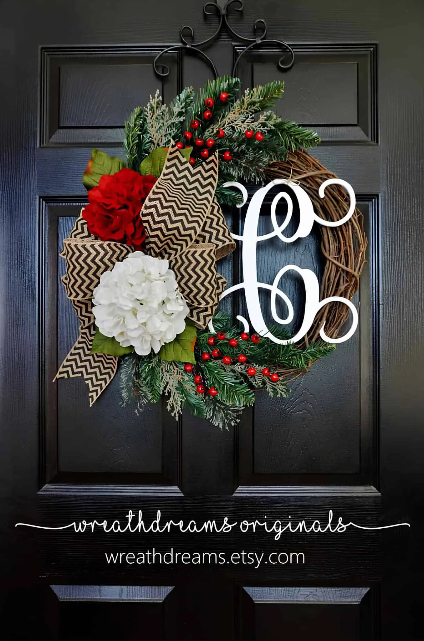 Holzkrone mit Chevron-Bogen und Hydrangeen-Monogramm Lebendige Feiertagskrone mit roten und weißen Blumen, Grünpflanzen sowie einem modernen „Ho Ho“-Schild, verziert mit Kiefernzapfen und Beeren, die an einer schwarzen Tür zum Weihnachtsfest hängt.