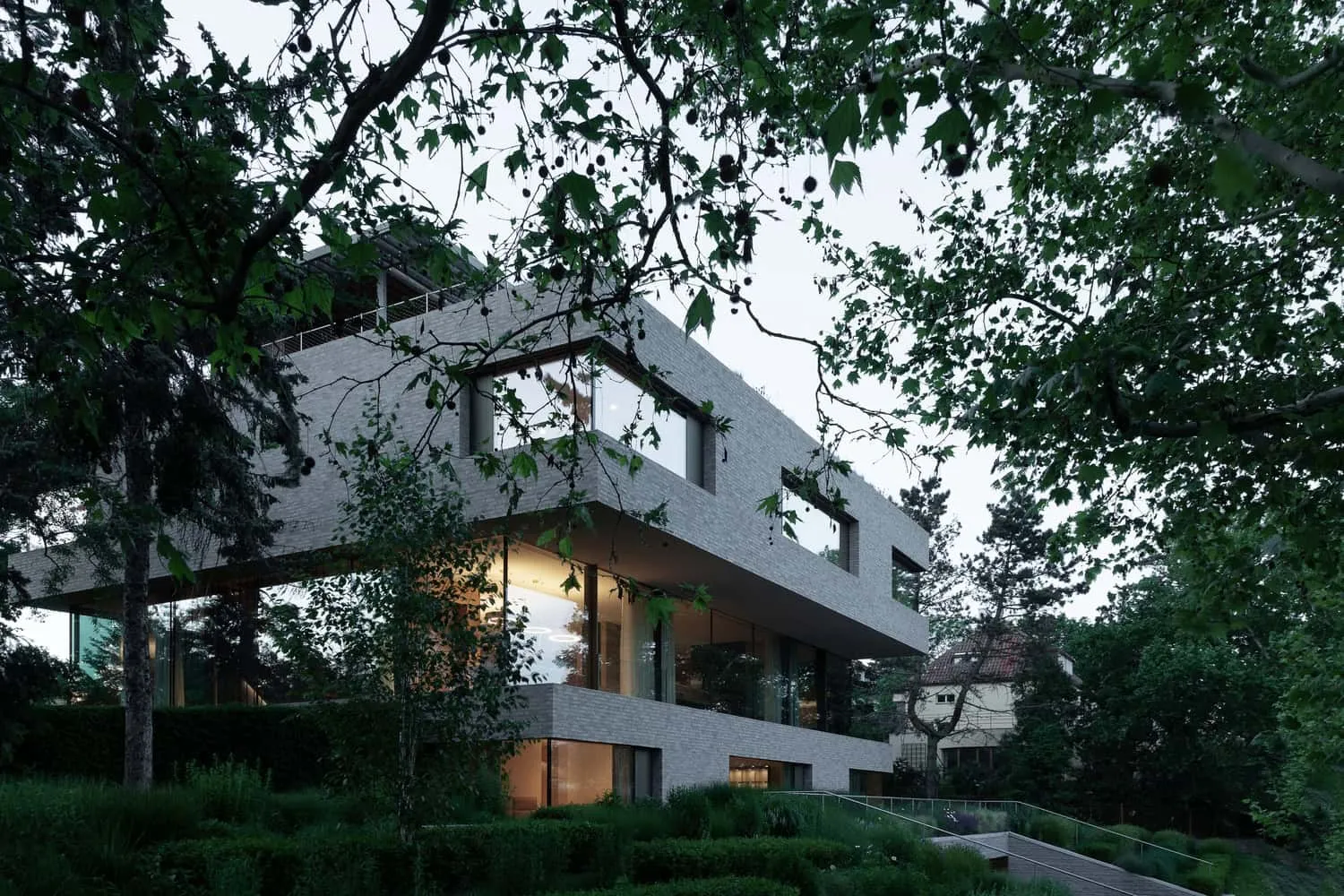 Villa Vista – Garten im Hintergrund, entworfen von Znameni Ctyr Architekti Villa Vista von Znameni Ctyr Architekti, Blick auf die Villa im Hintergrund, umrahmt von ausgewachsenen Bäumen und Garten in Prag