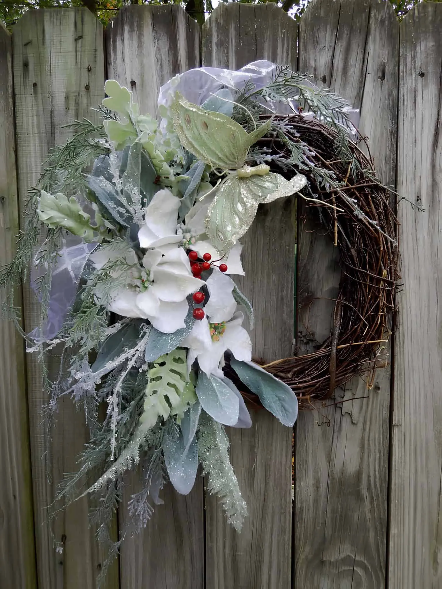 Holzkrone mit Schmetterling, Poinsettien und silberner Grünpflanzendekoration Holzkrone in Form eines Rebenrankens mit silberner Grünpflanzendekoration, weißen Poinsettien und einem dekorativen Schmetterling
