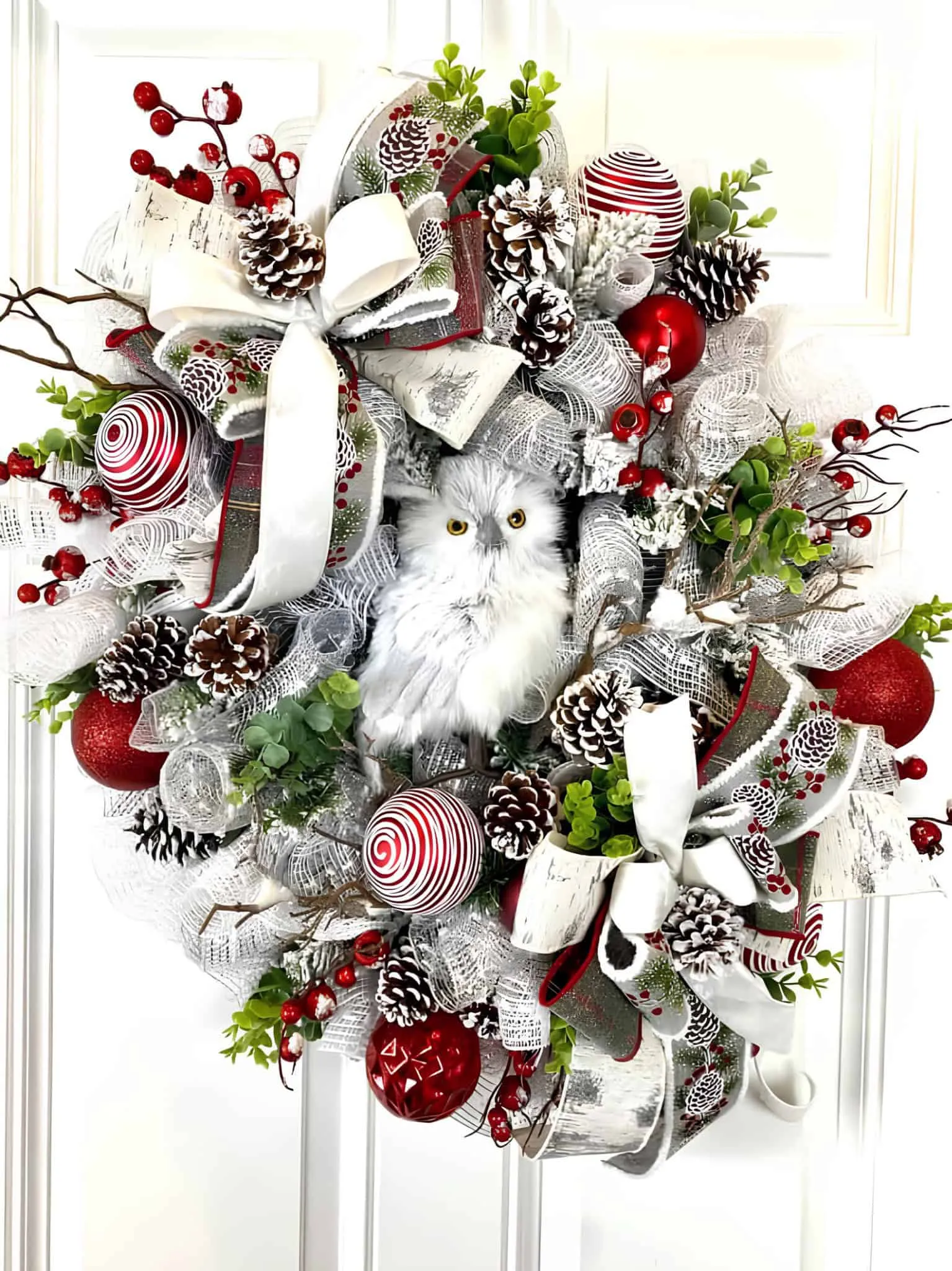 Schneeeule-Kranz mit Bändern zum Weihnachtsfest Weiße Schneeeule in einem roten und weißen Bänderkranz zum Weihnachtsfest mit Kiefernzapfen und Verzierungen