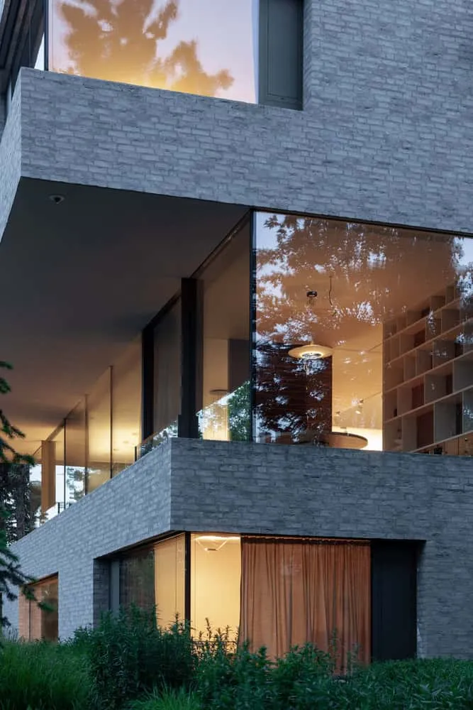 Bibliothek in der Ecke der Villa Vista mit Verglasung bei Dämmerung von Znameni Ctyr Architekti Villa Vista von Znameni Ctyr Architekti, Ecke mit Bibliothek und Wohnraum sowie großen verglasten Wänden bei Dämmerung