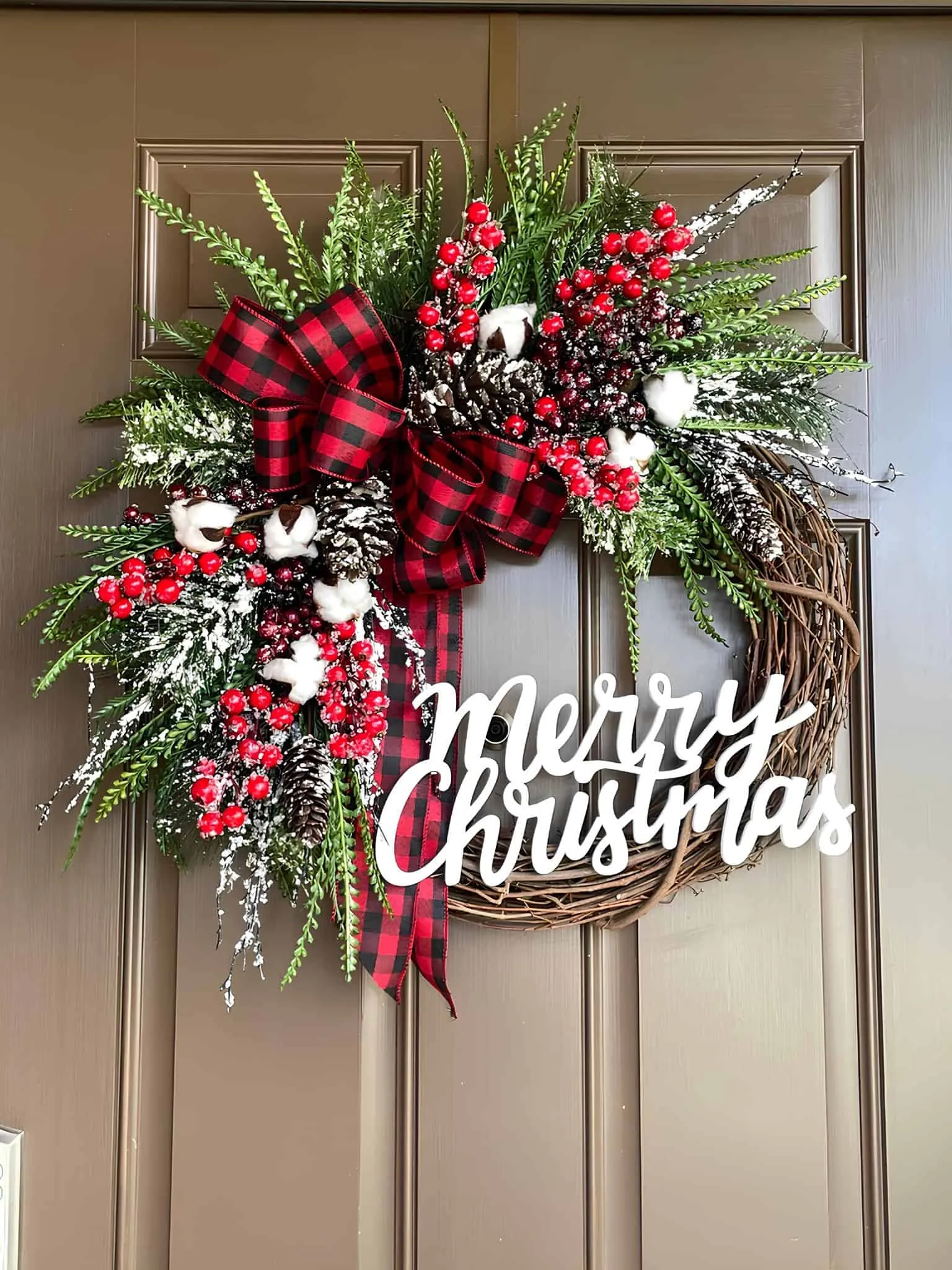 Fröhliche Weihnachten – Holzschild mit Buffalo-Plaid-Binde Holzene Weihnachtskranz mit Rebenmotiv, Buffalo-Plaid-Binde, Beeren, schneeweißen Grüntönen sowie einem Schild mit der Aufschrift ‚Fröhliche Weihnachten‘