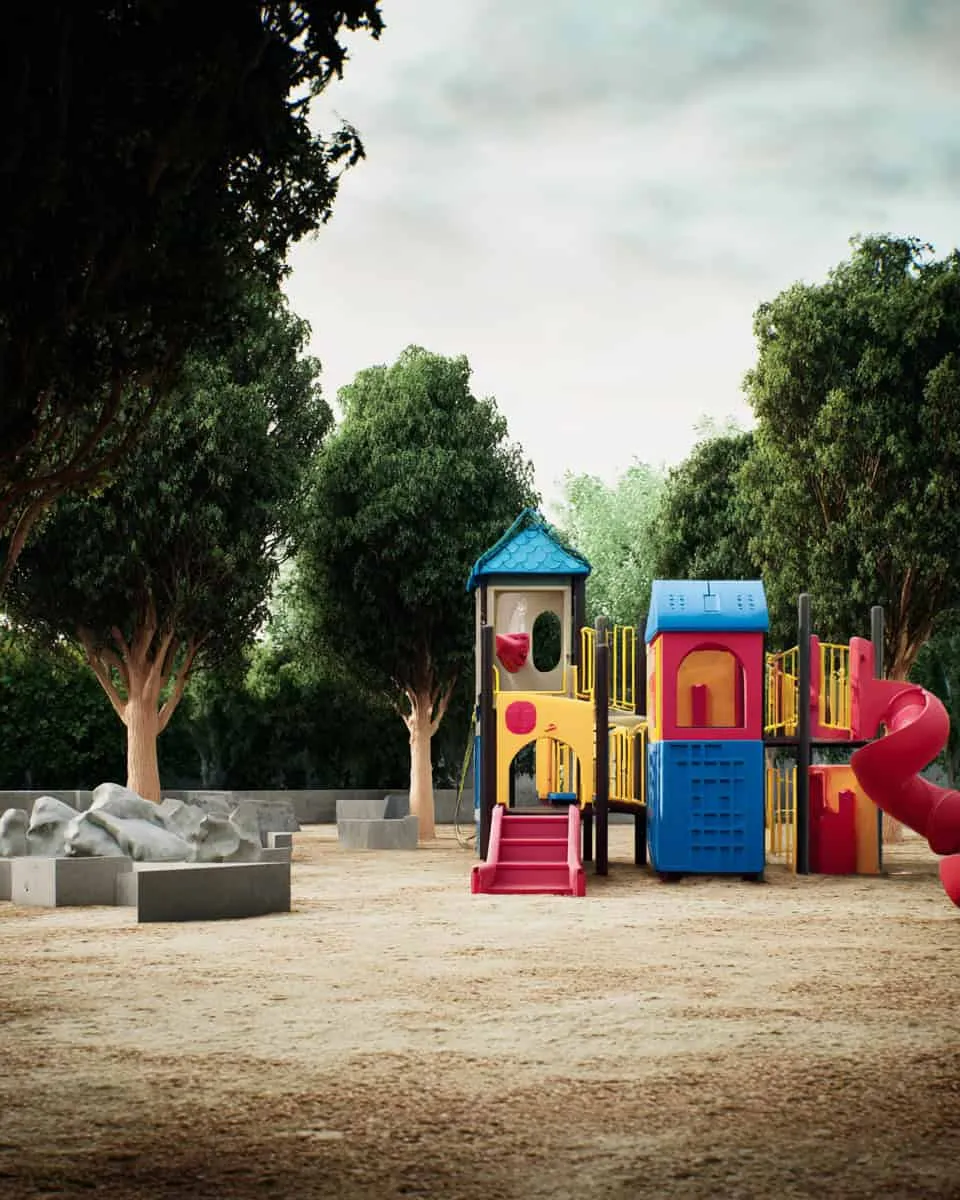 Colorful kids playground with slides and tunnels surrounded by lush green trees in a park setting.