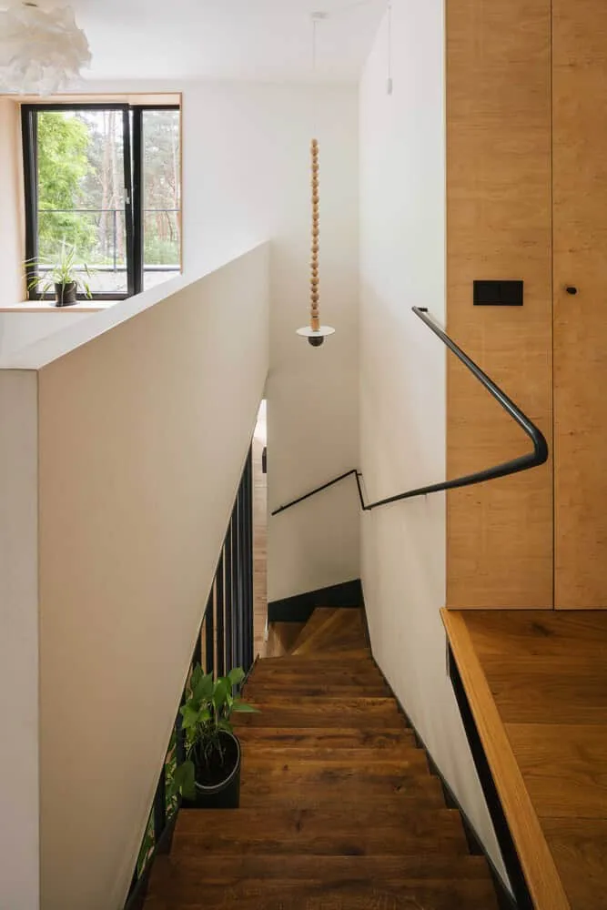 Treppe im Skubianka-Haus aus Holz von SZCZ Jakub Szczesny Ästhetische Treppe mit Holzstufen und modernem schwarzen Geländer in einem minimalistischen Wohninneren, natürliches Licht durch das Fenster, stilvolle Dekoration – ideal für Kunstentwürfe im Bereich der modernen Architektur.