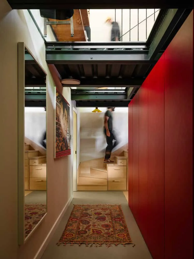 Dachfenster im Flur des Skubianka-Hauses von SZCZ Jakub Szczesny Heller moderner Innenraum mit Treppe und farbenfroher Kunst, ausgestattet mit Dachfenstern sowie glänzenden roten Wandakzenten, der moderne Architektur und innovatives Design für stilvolle Wohnräume veranschaulicht.