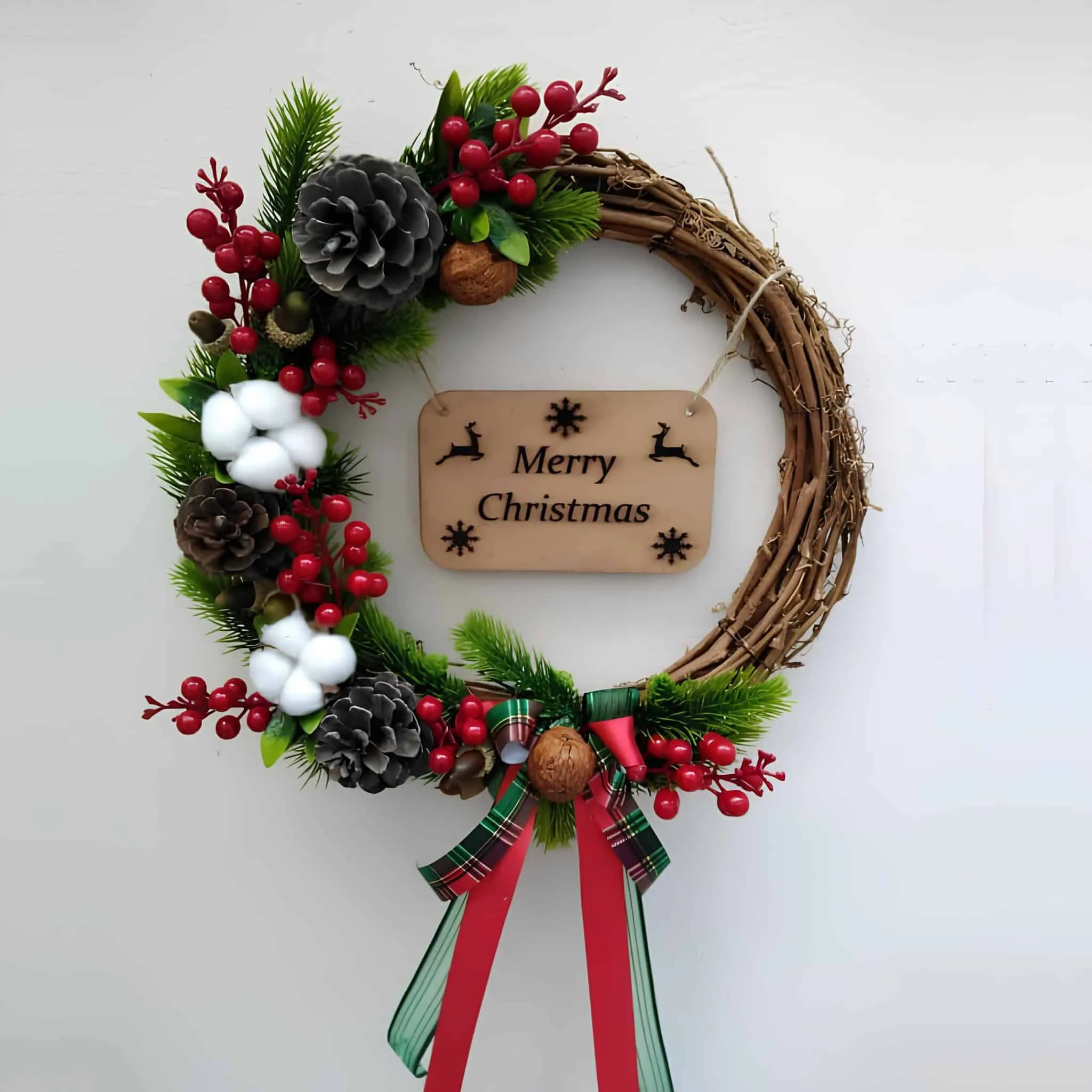 Frohe Weihnachten – Holzkranz mit Beeren und Kiefernzapfen Einfacher Holzkranz in Form eines Weinlaubs mit „Frohe Weihnachten“-Schild, roten Beeren, Baumwollkapseln und Kiefernzapfen