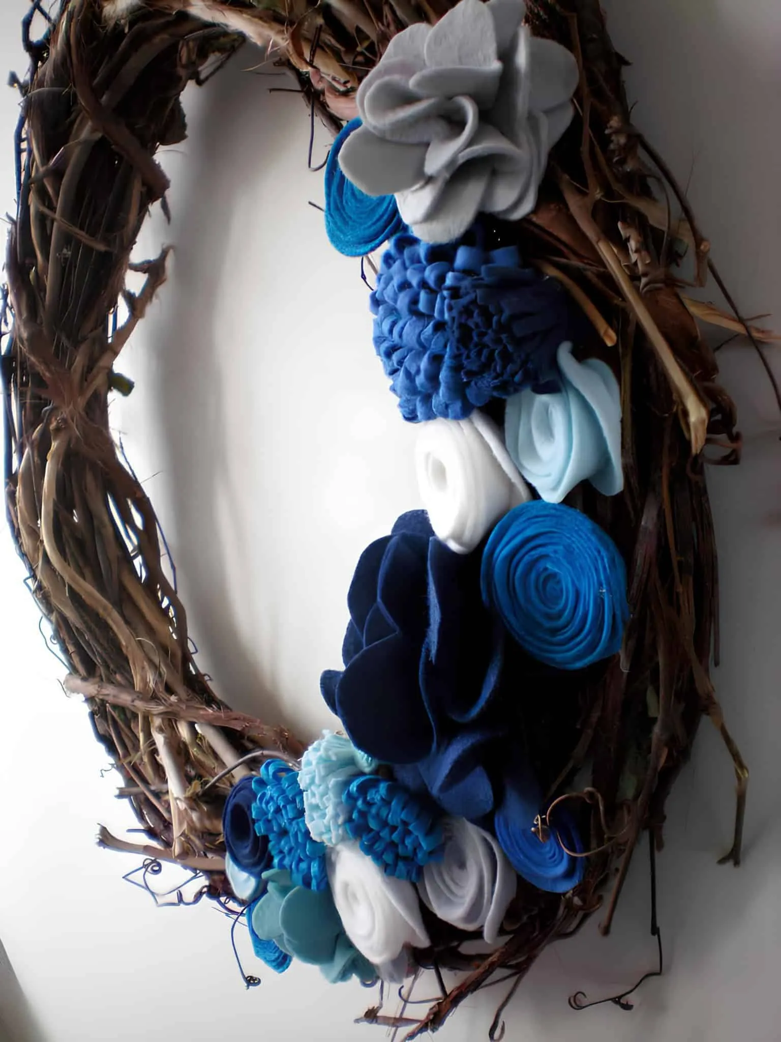 Blaue Filzblumen auf Holzkranz in Form einer Rebe Handgefertigter Holzkranz in Form einer Rebe, verziert mit blauen und weißen Filzblumen